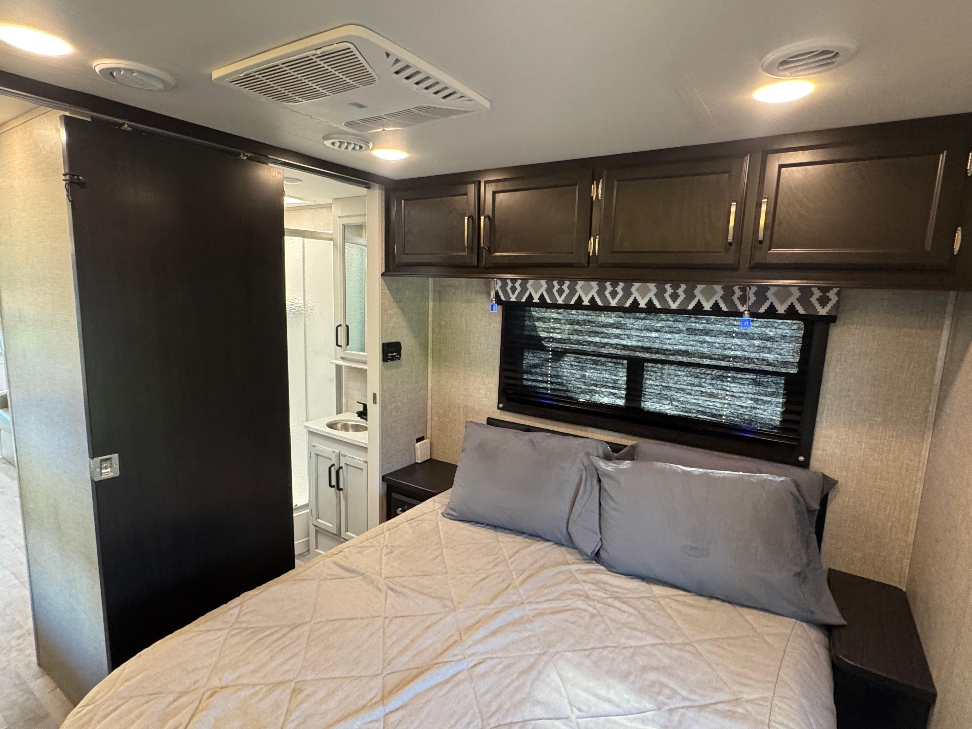 Inside an RV rental, this cozy bedroom features a quilted bed, overhead cabinets, and a sliding door to the compact bathroom.. Entegra Coach Odyssey 2022