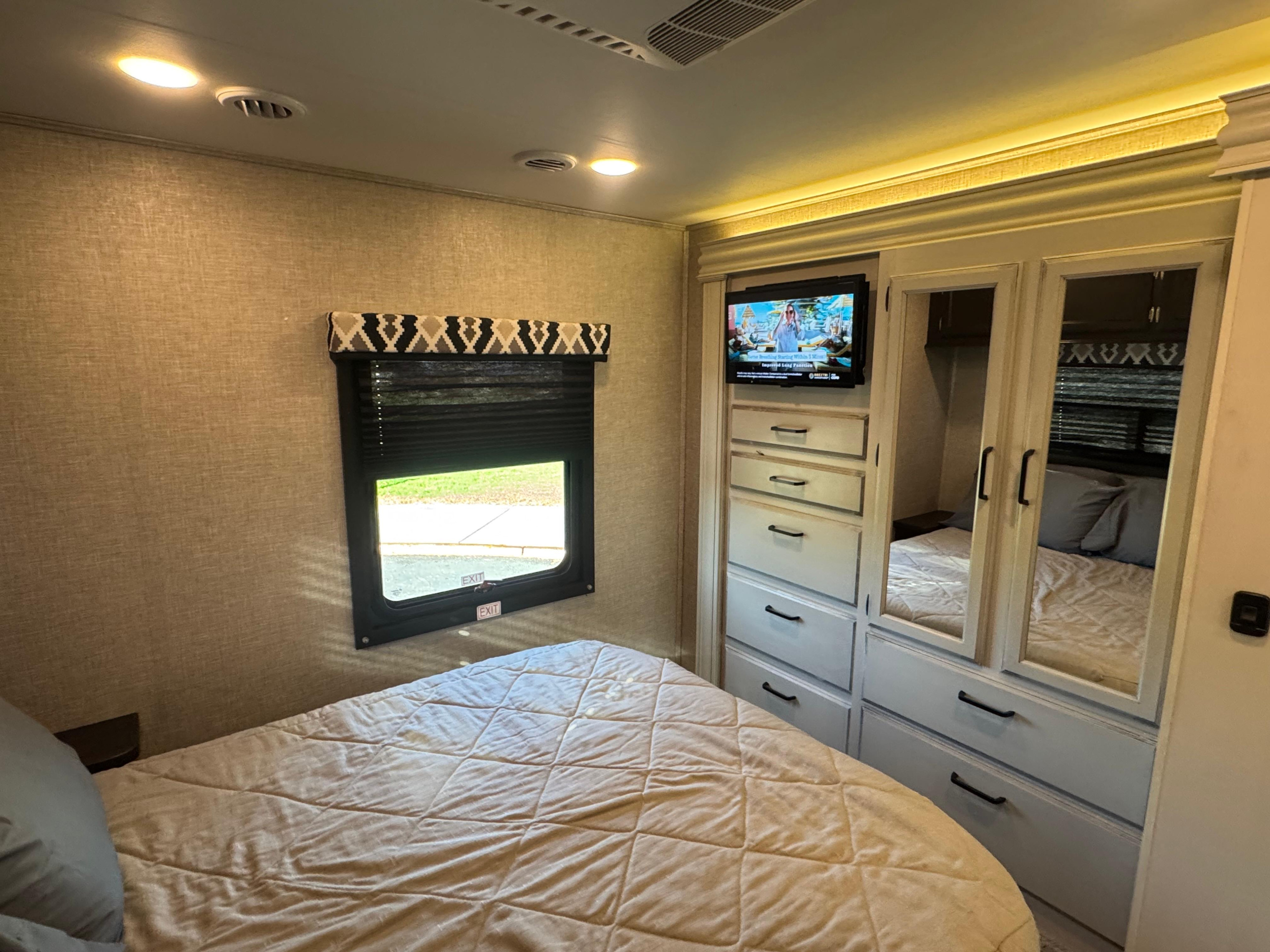 Inside a modern RV rental bedroom, featuring a light-colored bed, window, TV, and mirrored closet storage.. Entegra Coach Odyssey 2022