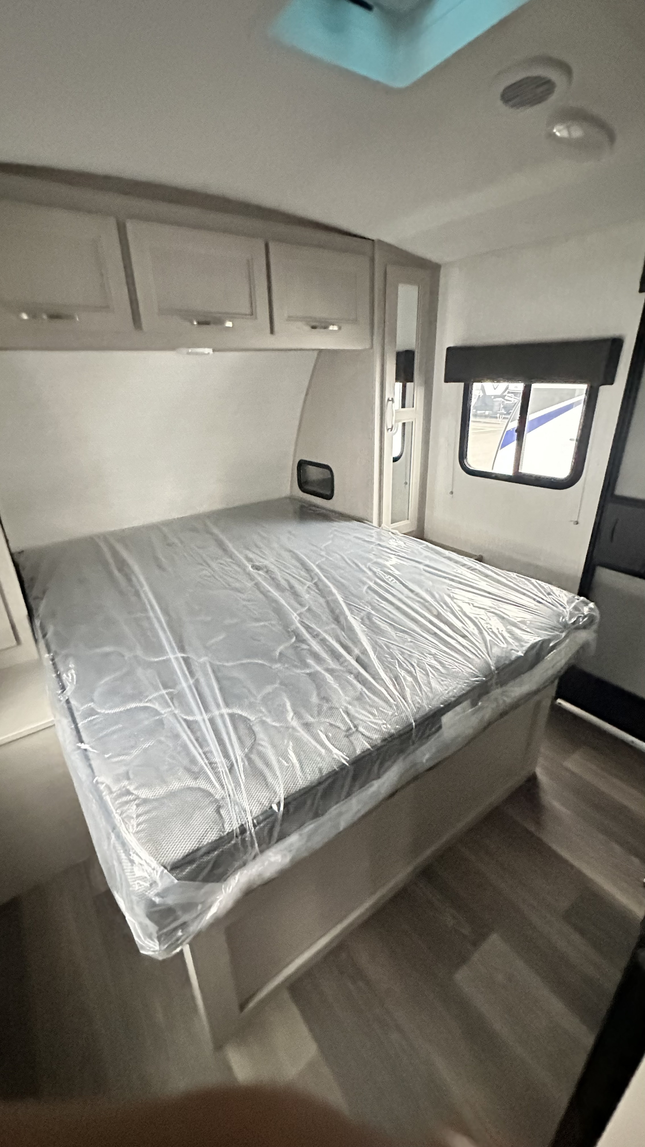 New RV rental bedroom: plastic-covered mattress, overhead storage, window with blind, mirror, and wood floor.. Cruiser RV Shadow Cruiser 2024