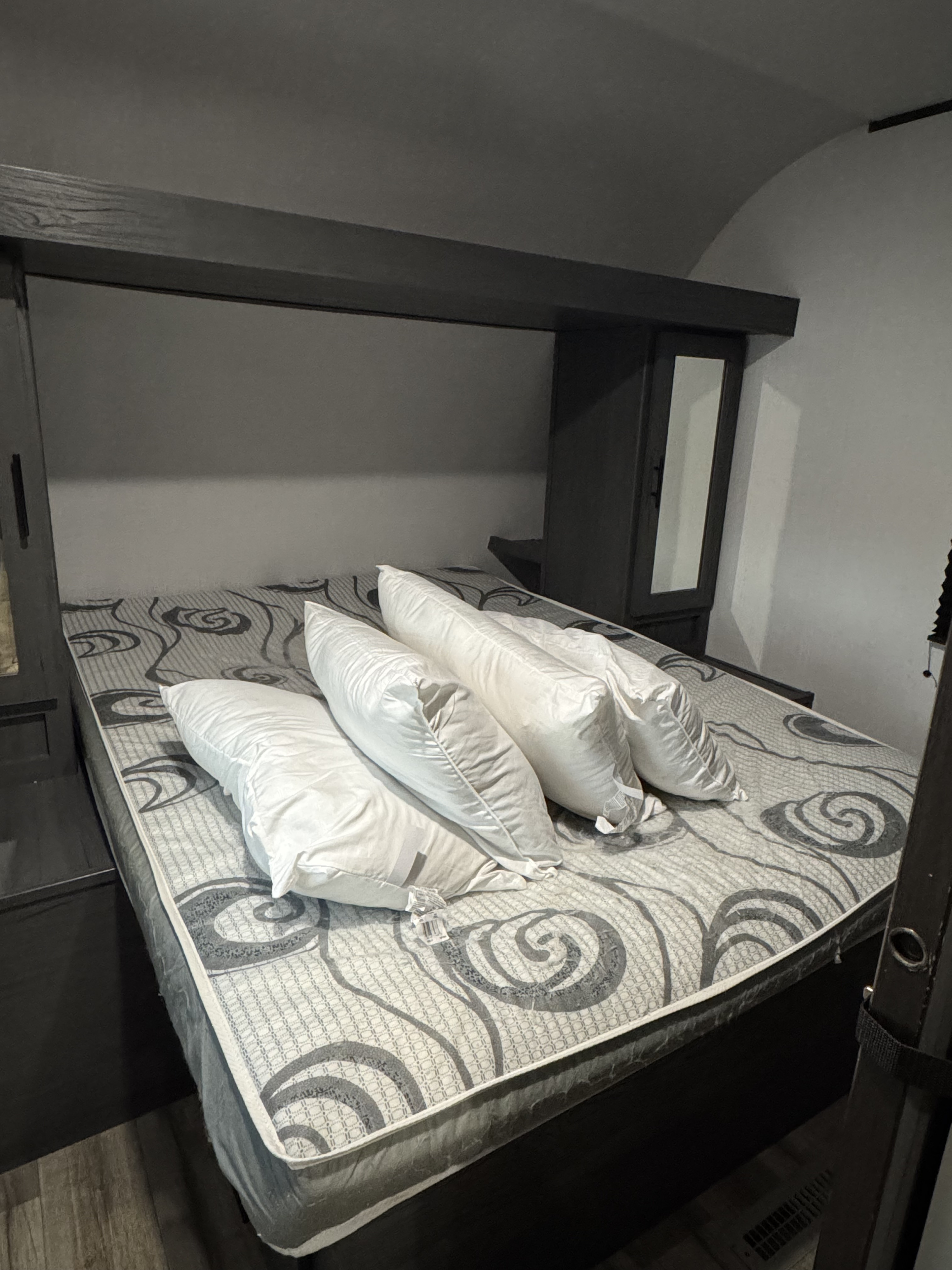 RV rental bedroom featuring a full bed with a patterned mattress and four white pillows, framed by dark wood cabinetry.. Na Na 2025