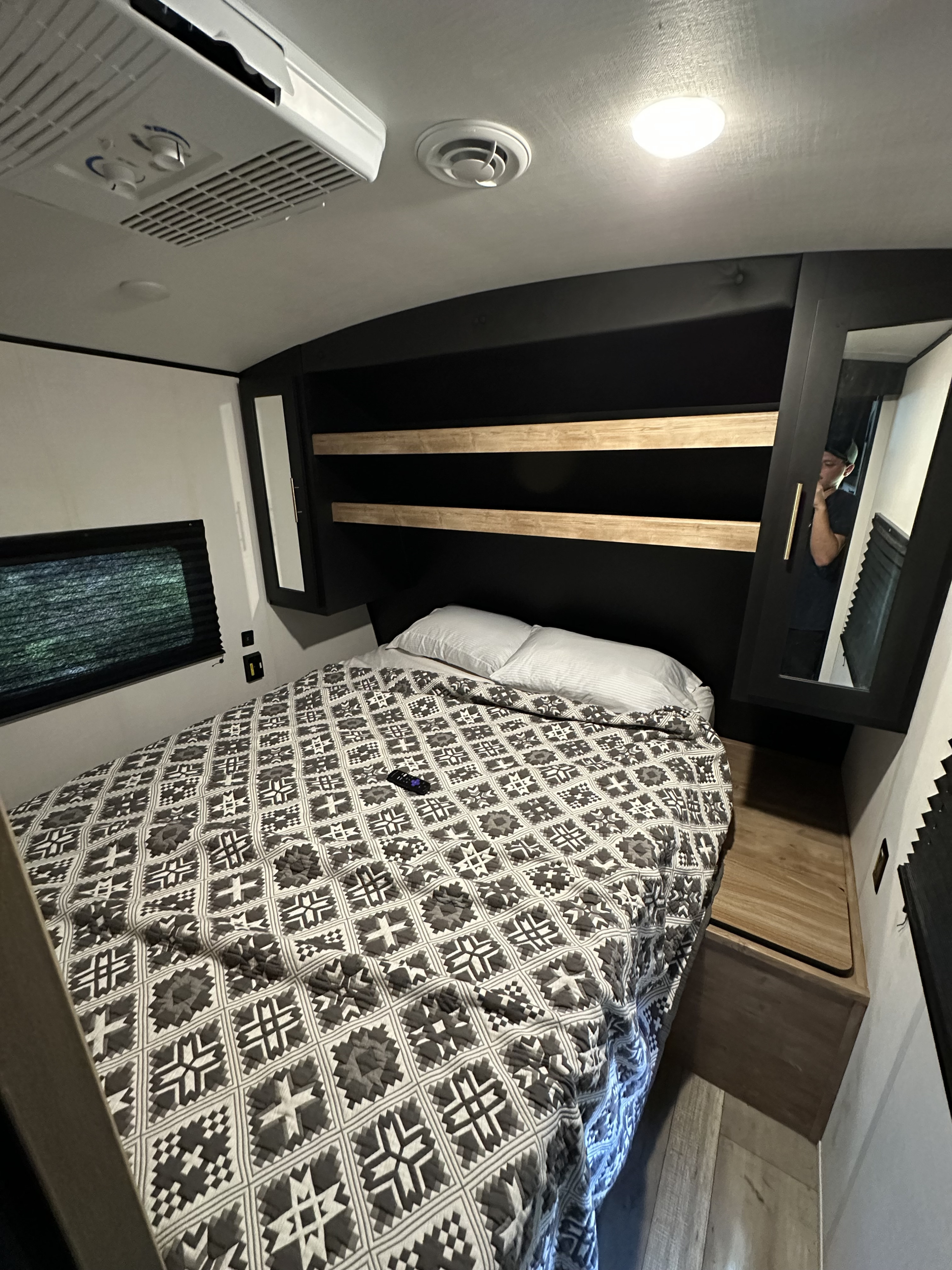 RV rental bedroom featuring a patterned bed, storage shelves, and mirrored wardrobe, showing a cozy and functional space.. Keystone RV Springdale 2023