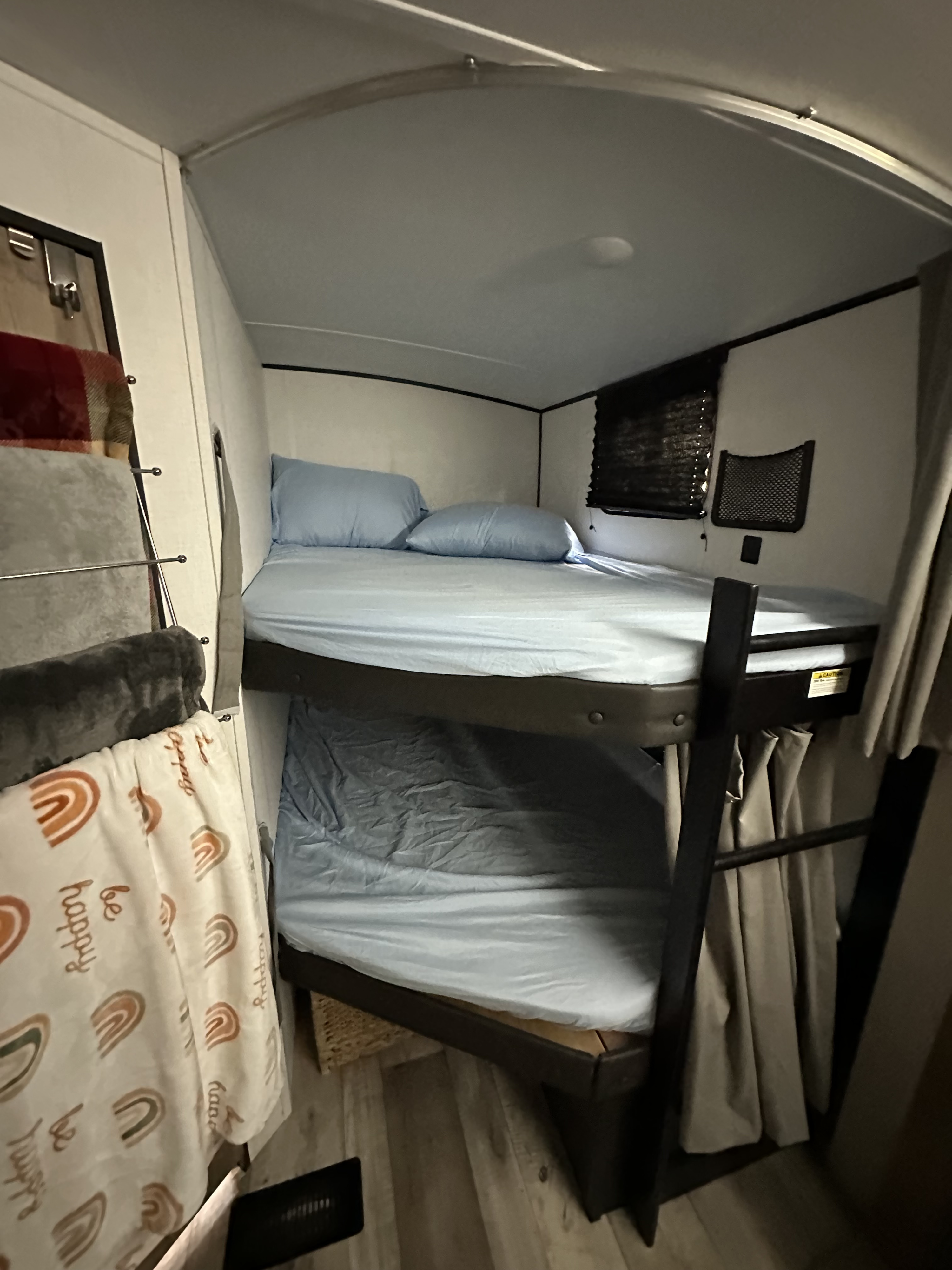 RV rental bunk beds with blue sheets and pillows, a ladder, and wall storage, offering cozy sleeping space.. Keystone RV Springdale 2023