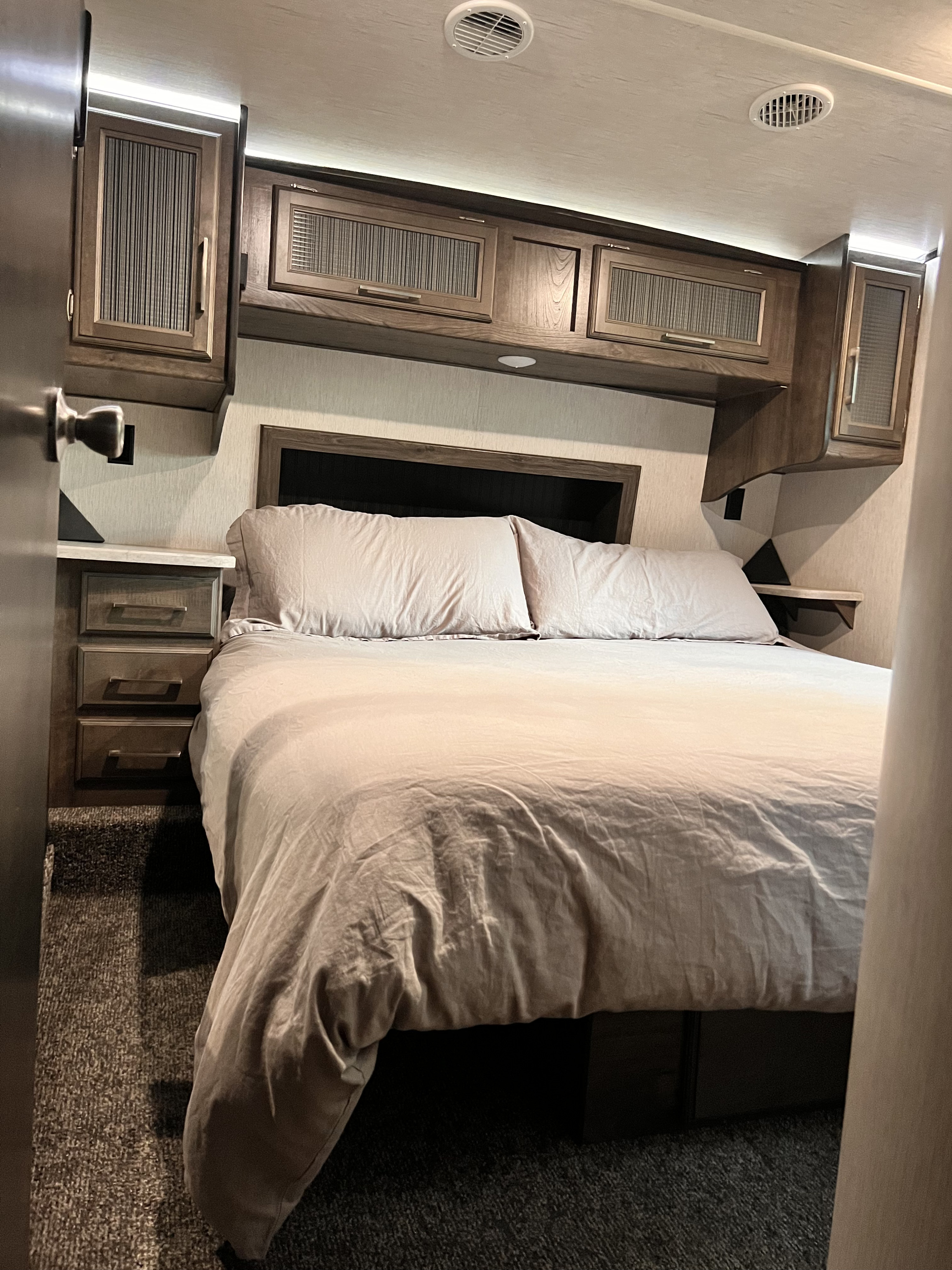 Cozy RV rental bedroom with comfortable bed, overhead cabinets, and soft lighting, offering a relaxing retreat.. Heartland Torque 2018