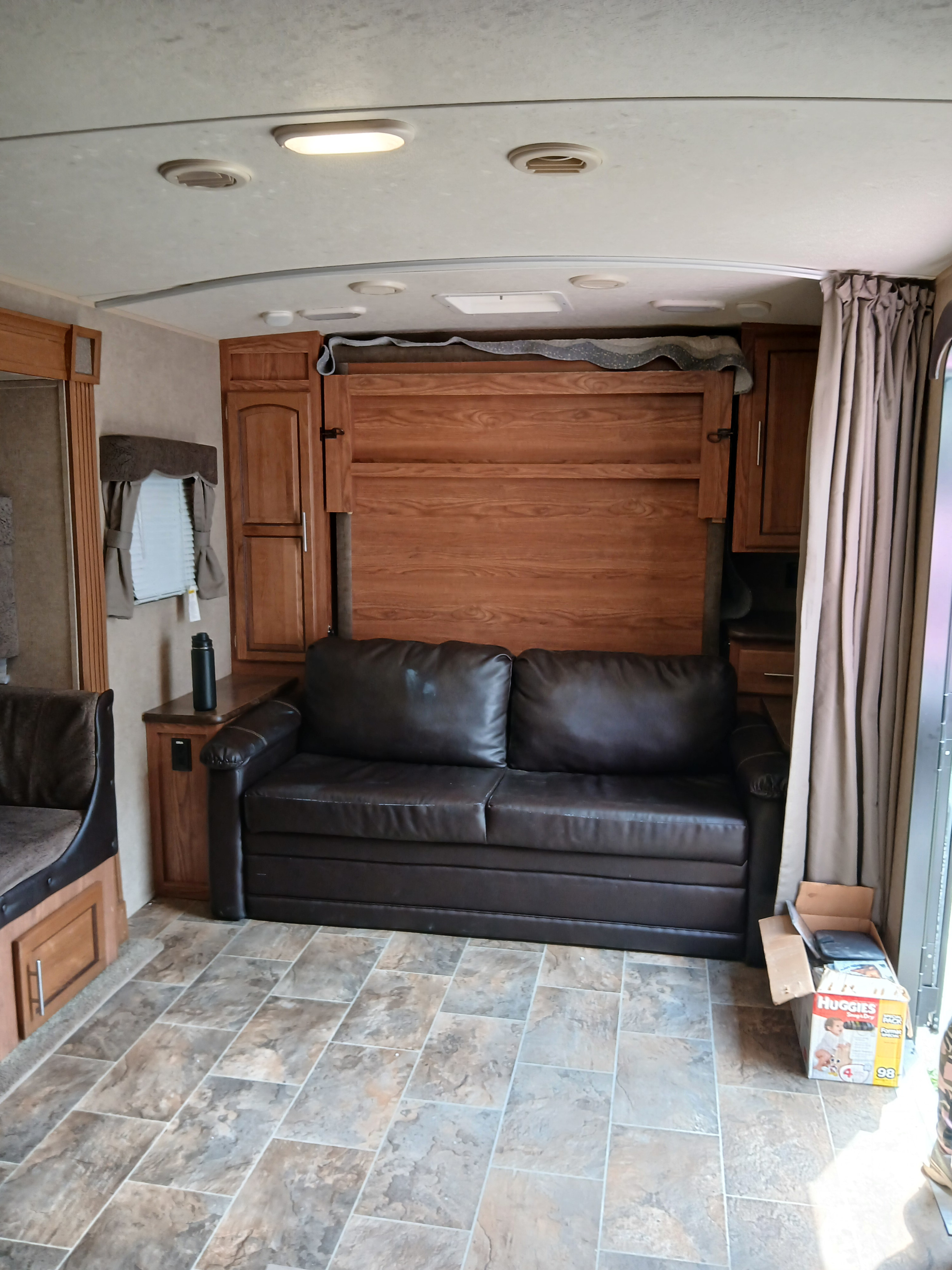 RV rental: Living area with folded wood murphy bed, brown sofa, and tiled floor, showcasing a compact design.. Forest River Rockwood Ultra Lite 2016