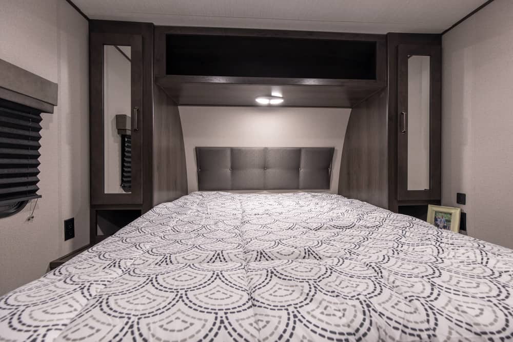 Comfortable RV rental bedroom with a large bed, built-in storage, padded headboard, and overhead lighting for travel.. xpolar 265bh 2023
