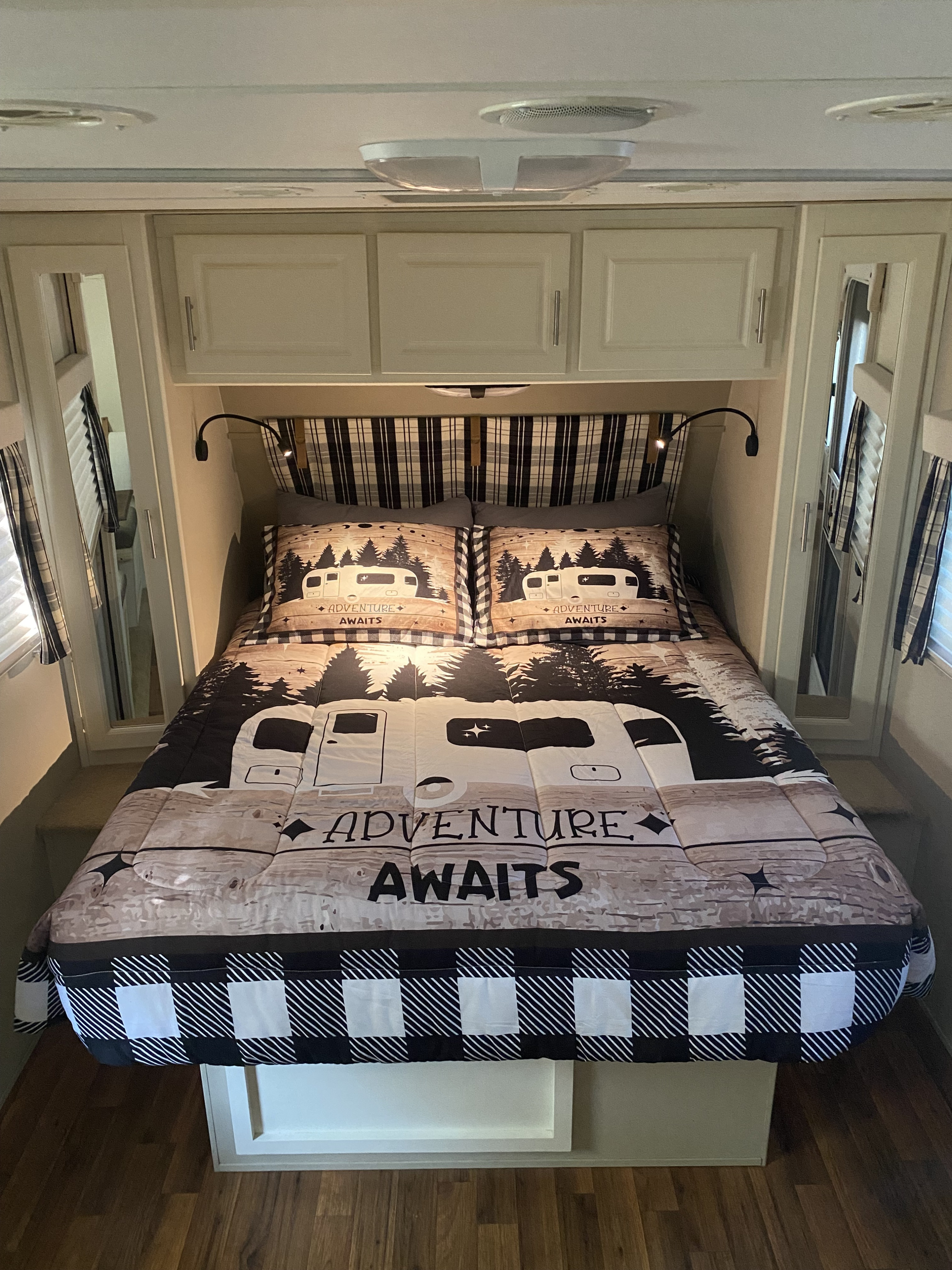 Cozy RV rental bedroom featuring "Adventure Awaits" bedding with camper design, plaid headboard, and overhead storage.. Cruiser RV Fun Finder X 2011