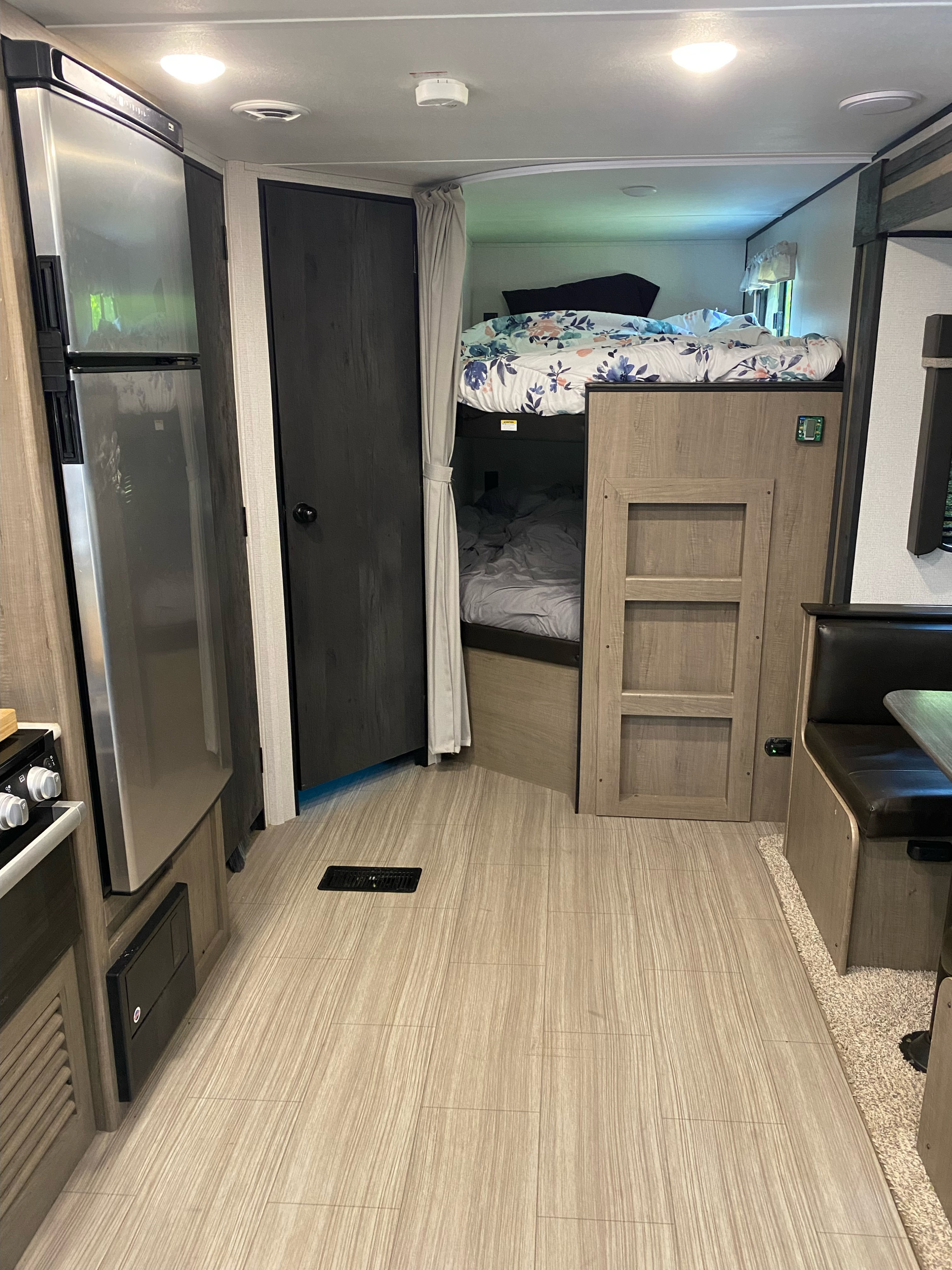 RV rental interior showcasing a stainless steel fridge, bunk beds with floral bedding, and a cozy dinette setup.. Keystone RV Hideout 2021