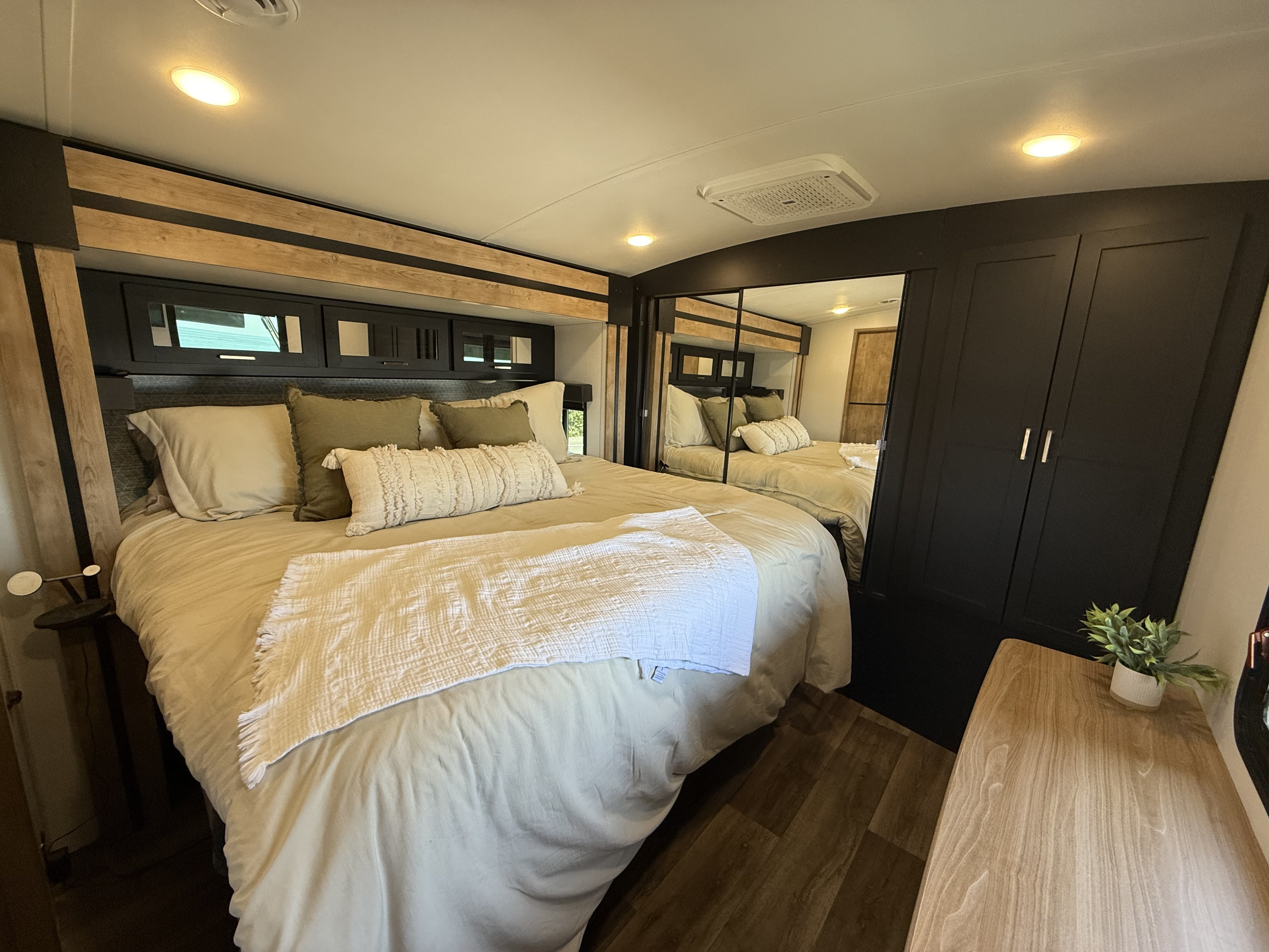 Modern RV rental bedroom featuring a large bed, stylish dark cabinets, mirrored closet, and wood flooring.. Keystone RV Outback 2023
