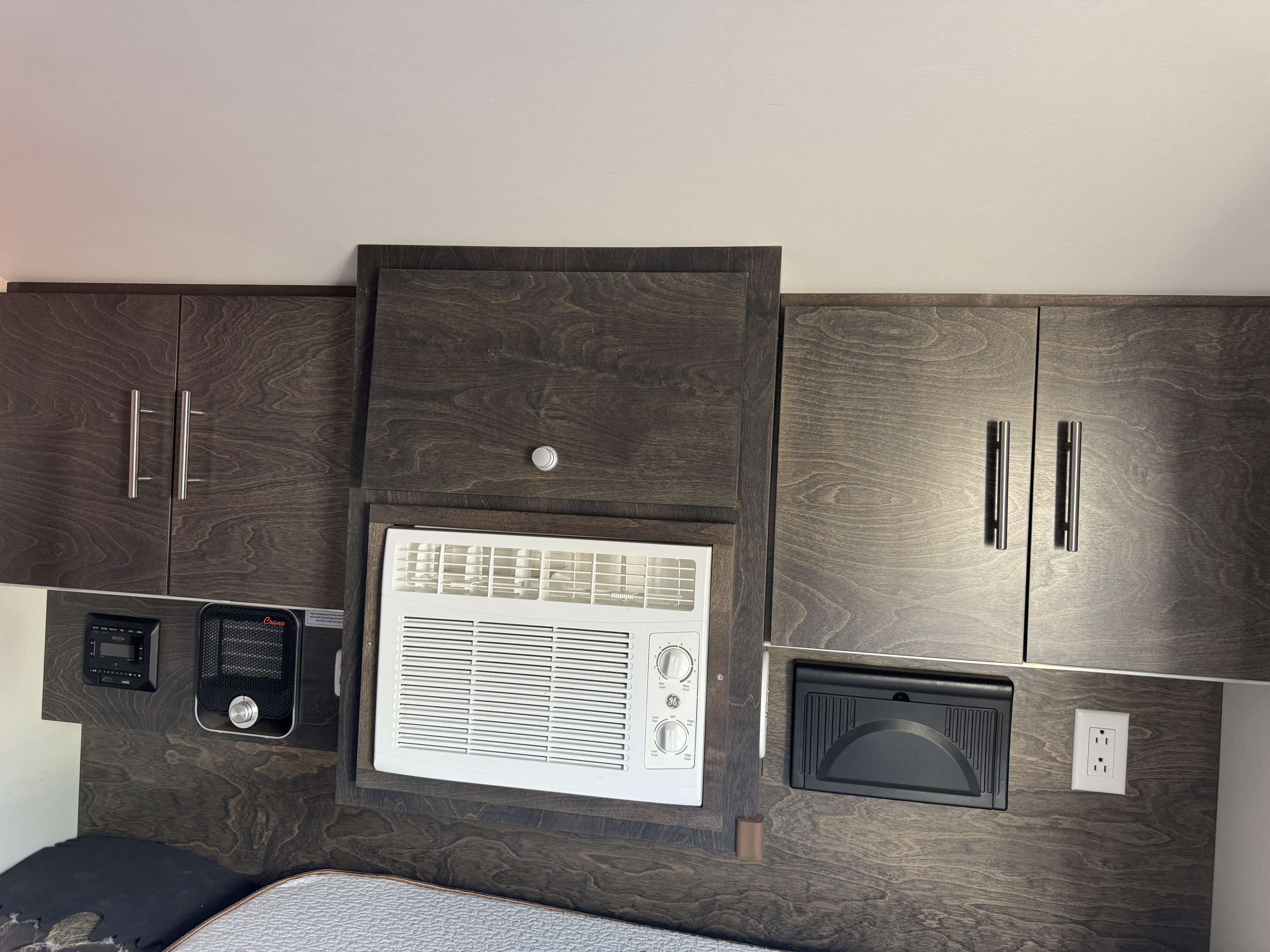 This RV rental features dark wood grain cabinets, a window AC unit, heater, and entertainment controls for a comfortable stay.. nuCamp T@G 2021