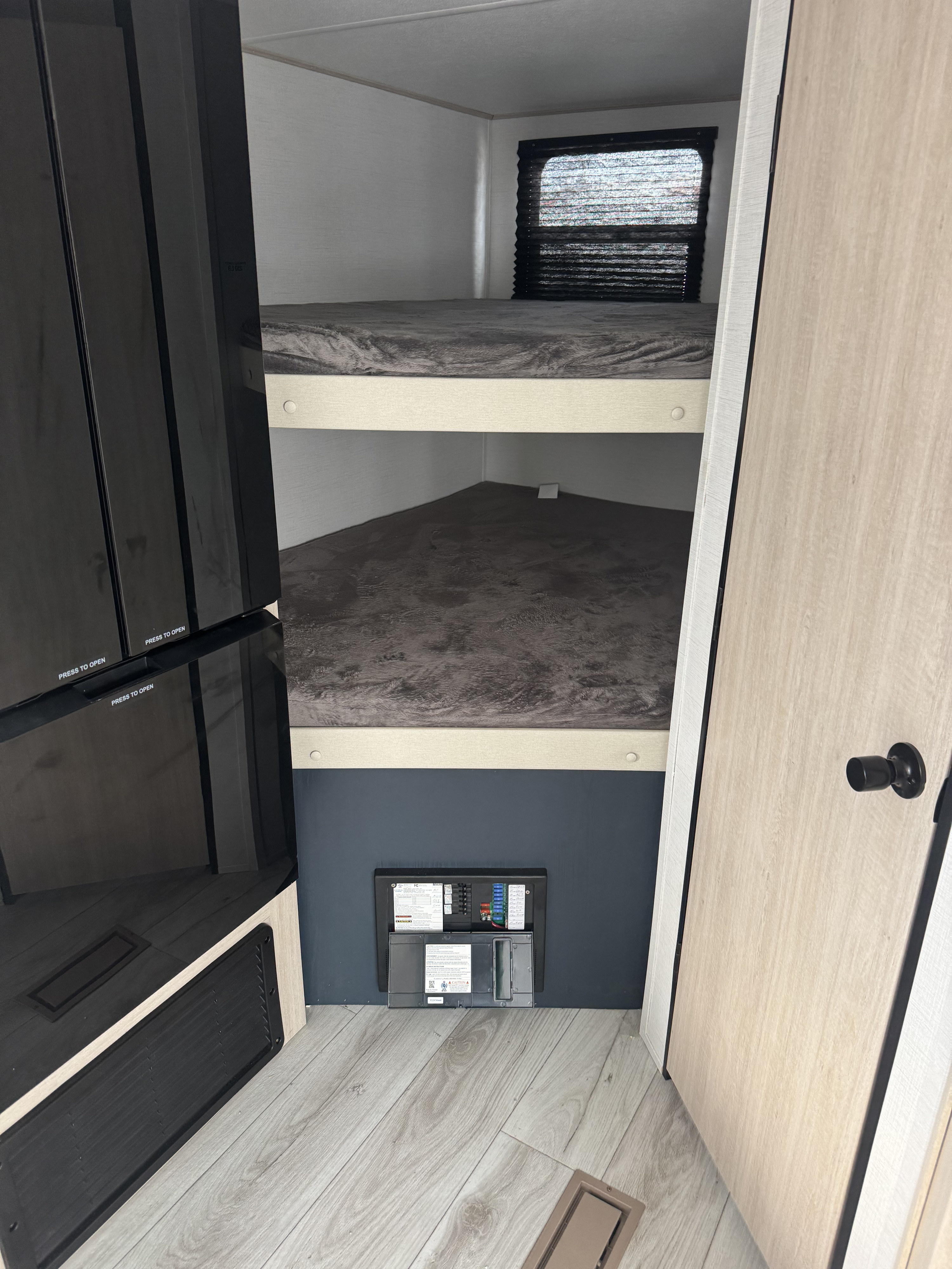 RV rental interior: two bunk beds with grey bedding, a black appliance, and an electrical panel. Cozy, functional sleeping space.. Prime Time Manufacturing Avenger LE 24BHSLE 2025