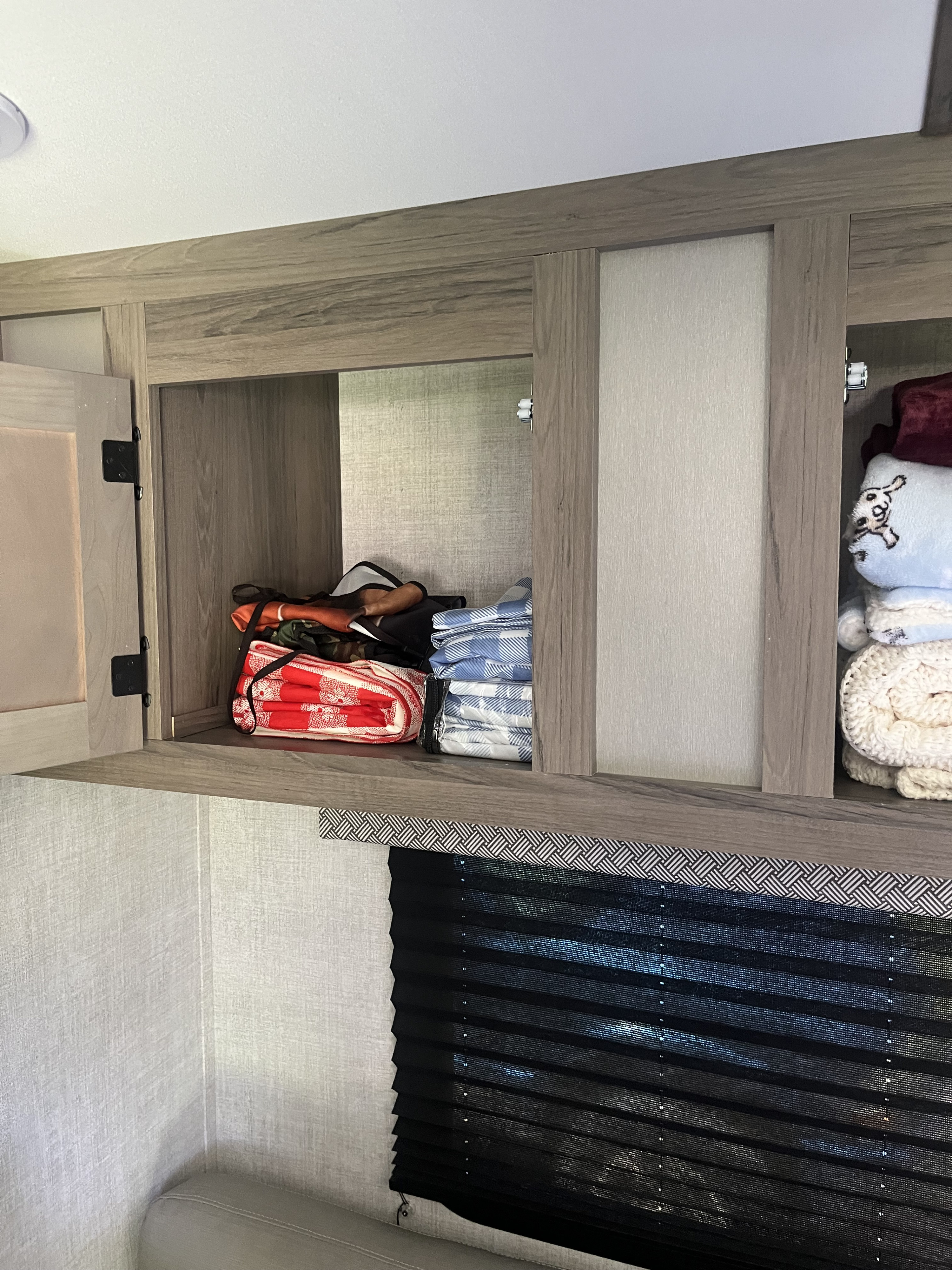 Inside an RV rental: open overhead cabinet storing blankets above a black blind.. Gulf Stream Ameri-Lite Super Lite 2022