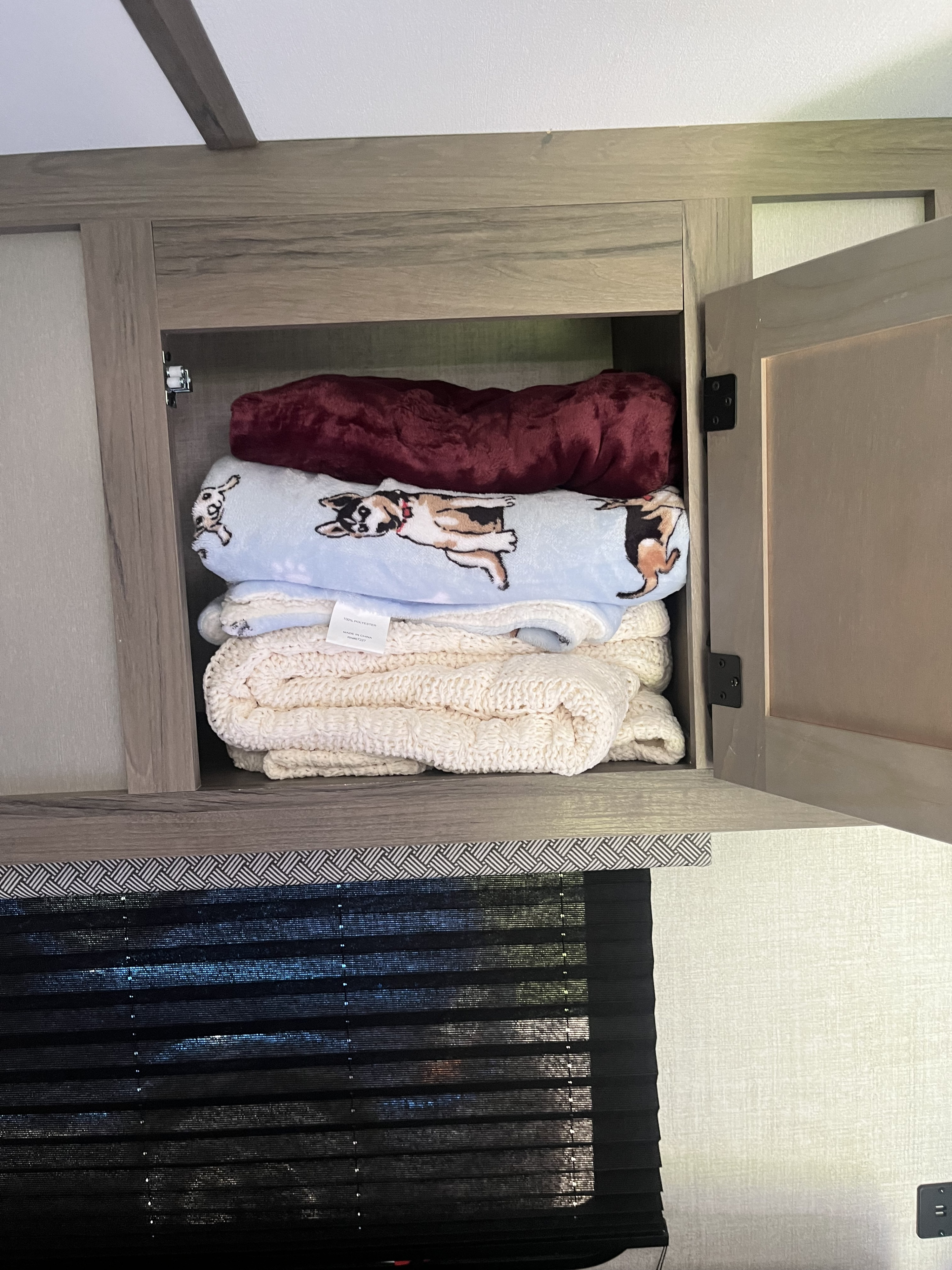 Inside an RV rental: a cabinet filled with stacked cozy blankets, including a dog-patterned one, for comfort.. Gulf Stream Ameri-Lite Super Lite 2022
