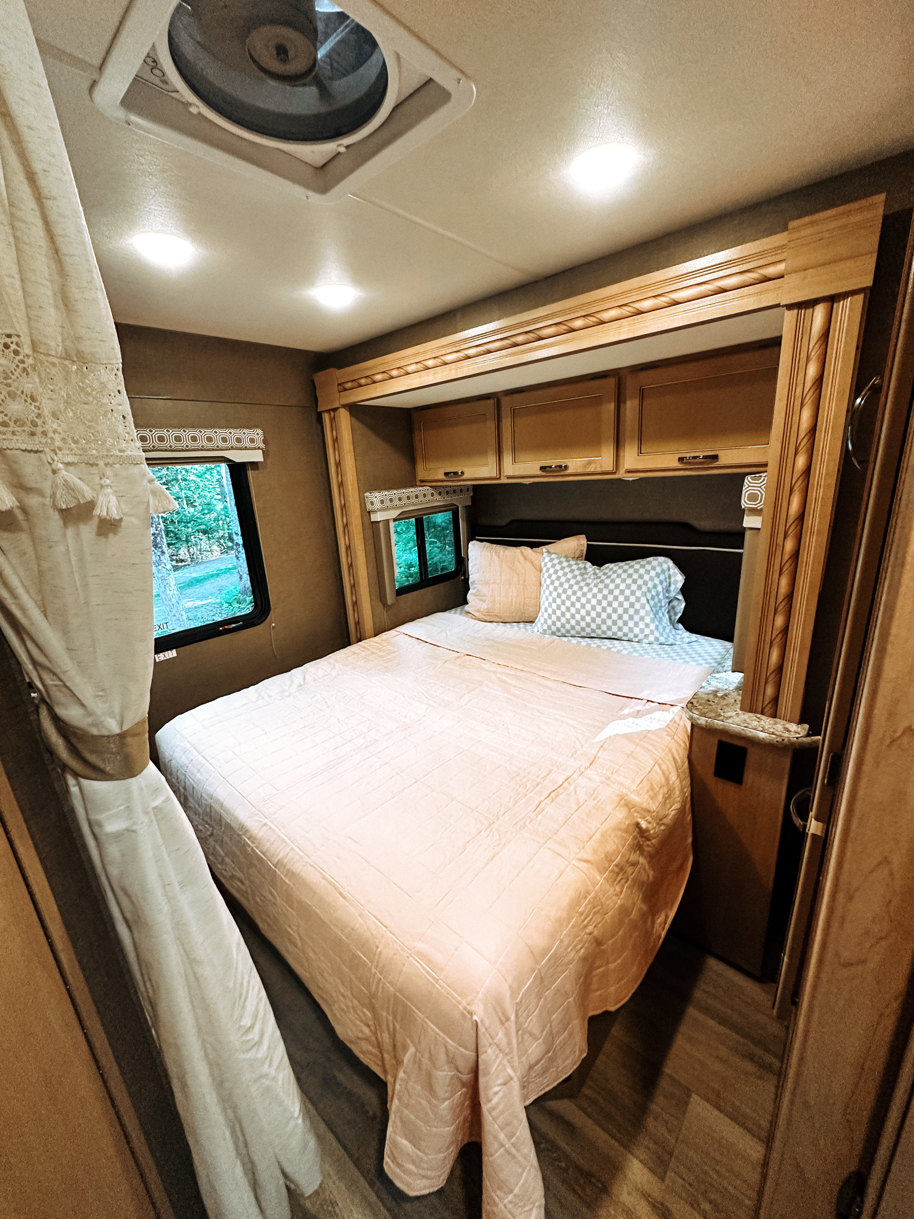 Spacious RV rental bedroom with soft peach bedding, overhead cabinets, and a scenic window view.. Thor Four Winds 2018