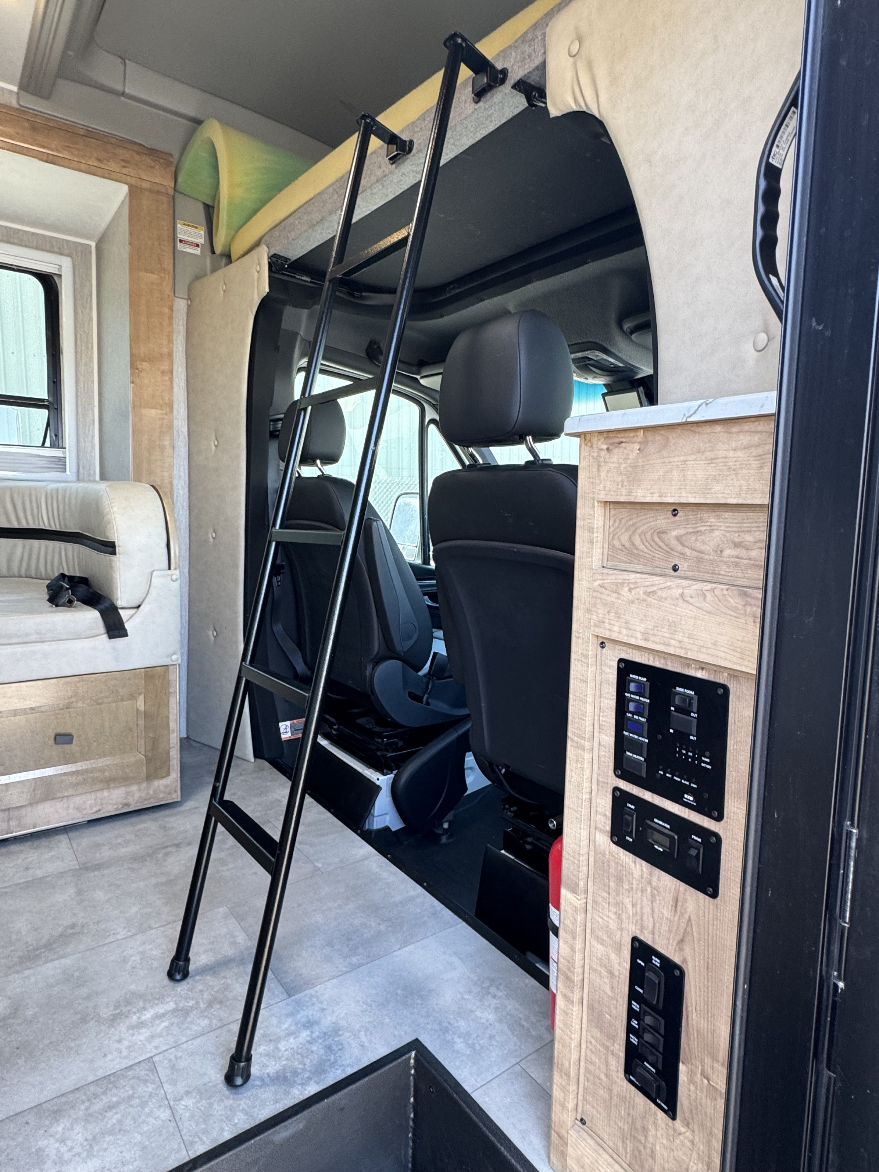 An RV rental interior with a ladder to an upper sleeping area above the driver's seats, plus a couch and control panel.. Coachman Prism Select 24 CB 2021