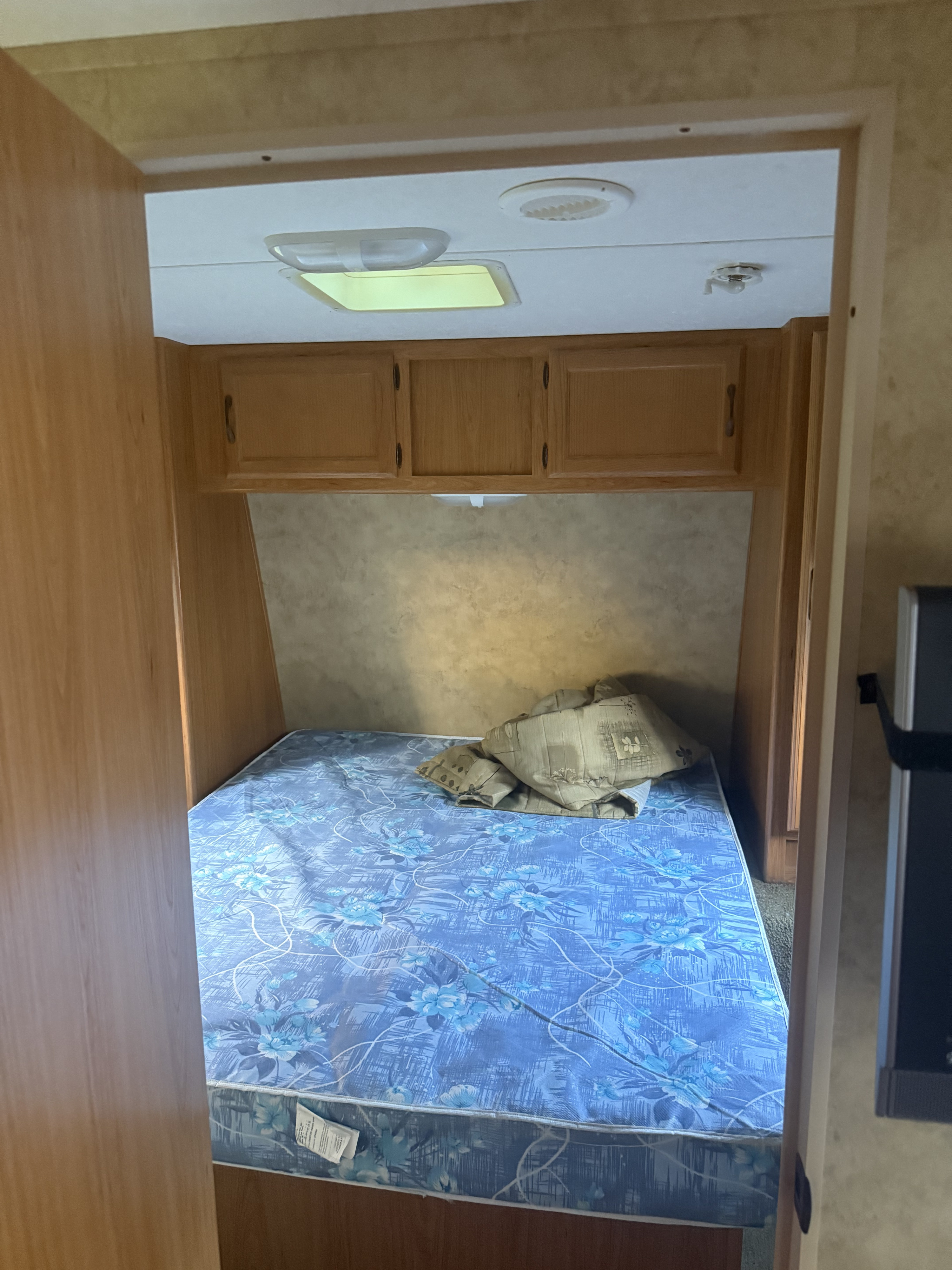 Cozy RV rental bedroom featuring a blue floral mattress, overhead wooden cabinets, and ceiling lights.. Keystone RV Hornet 2009