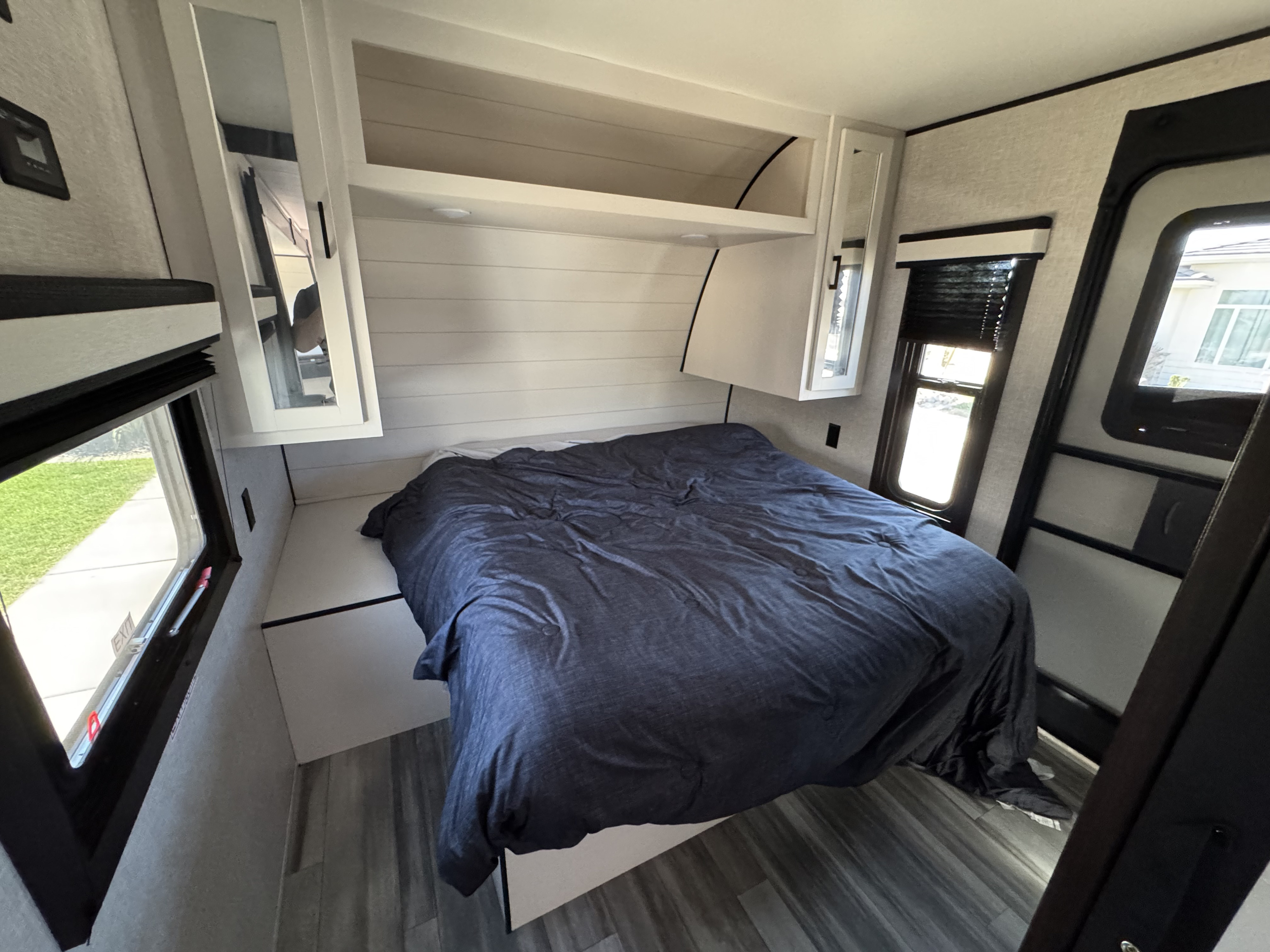 RV rental bedroom with a blue bed, overhead white shiplap cabinets, and windows on both sides for natural light.. Jayco Jay Flight 2024