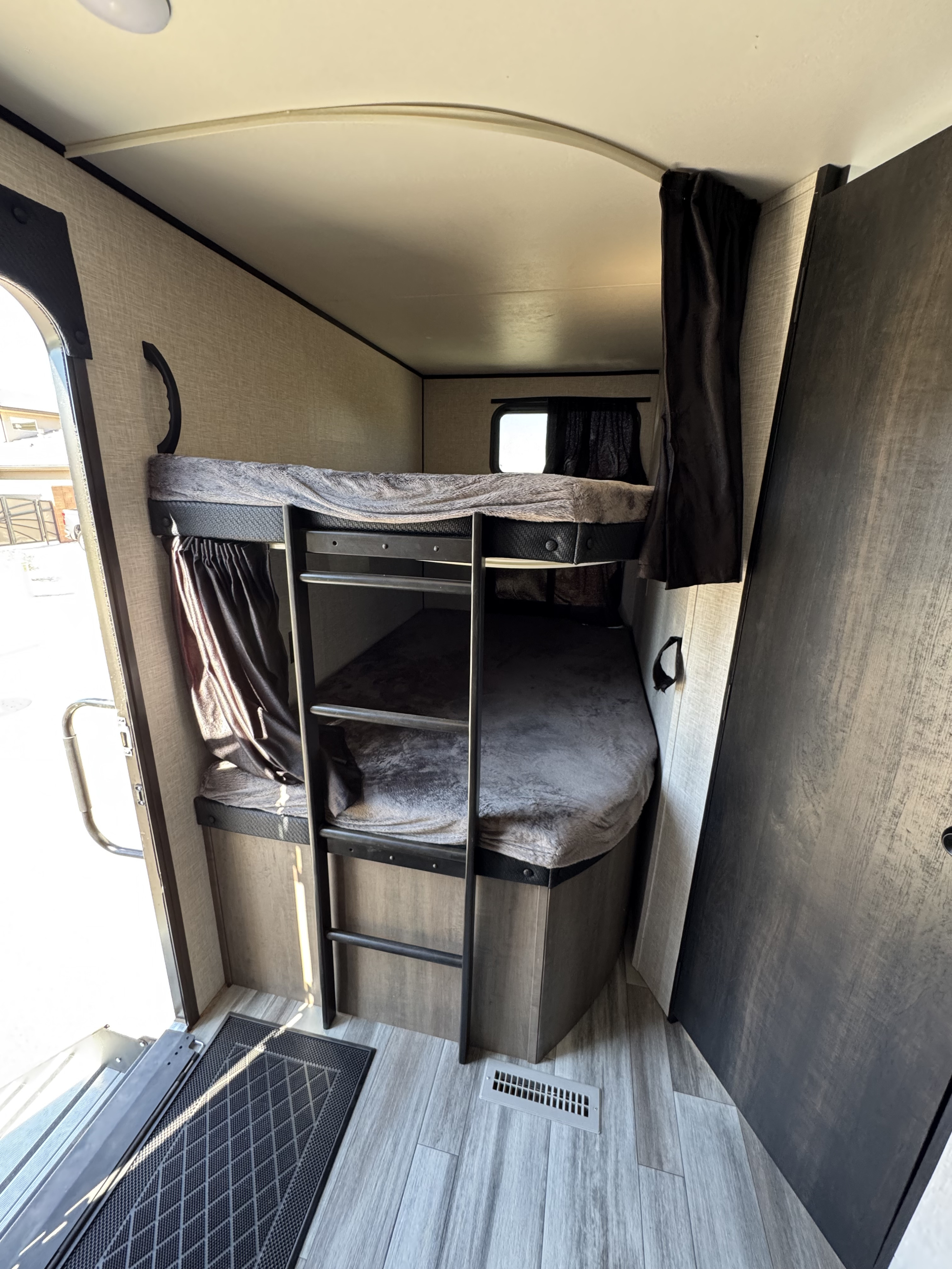 Explore a compact RV rental interior featuring cozy bunk beds with soft grey blankets, a ladder, and light wood-look flooring.. Jayco Jay Flight 2024