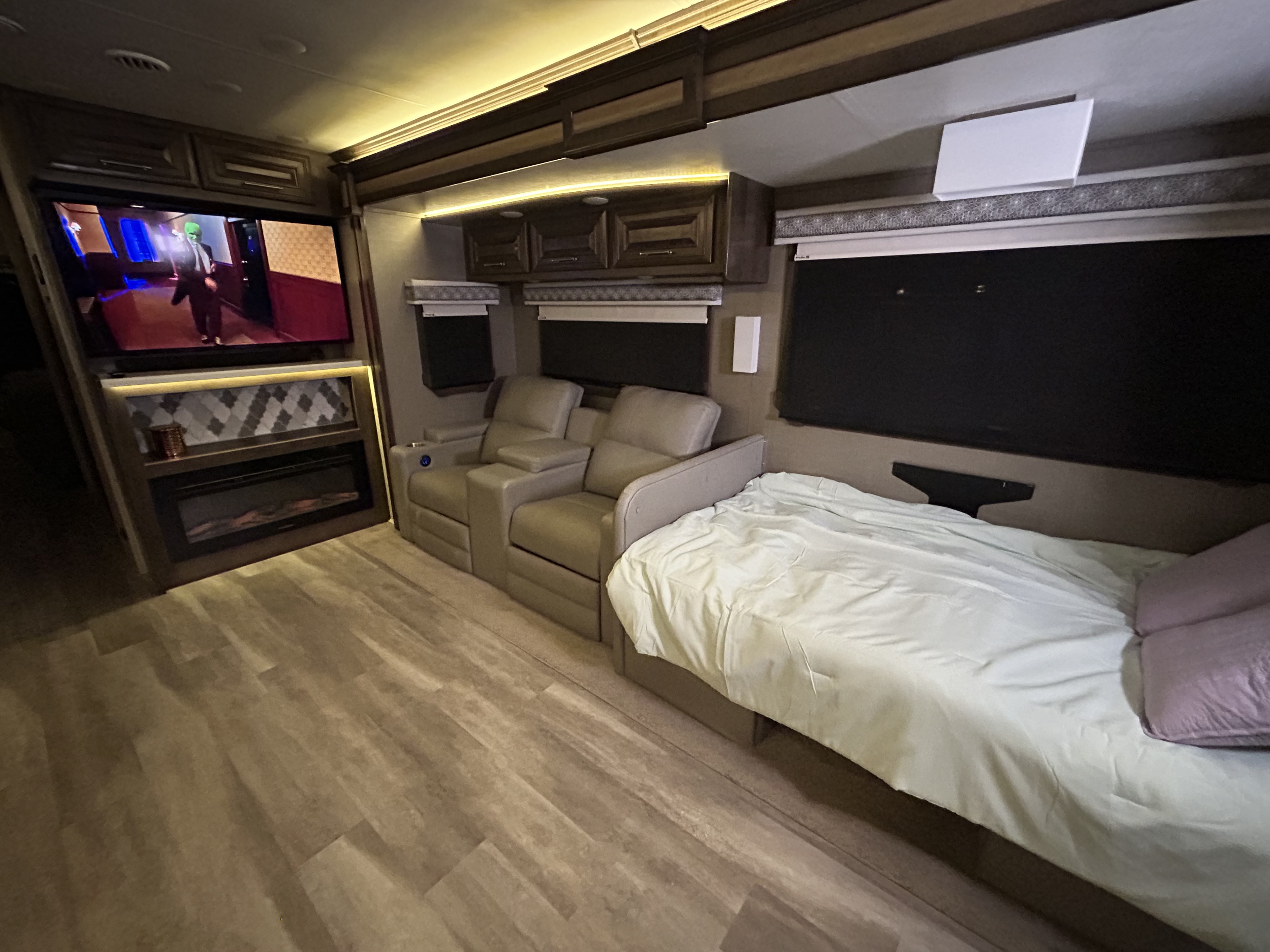 Modern rv rental interior: TV displaying "The Mask," plush recliners, a comfortable bed, and warm ambient lighting.. Entegra Coach Accolade XL 2022