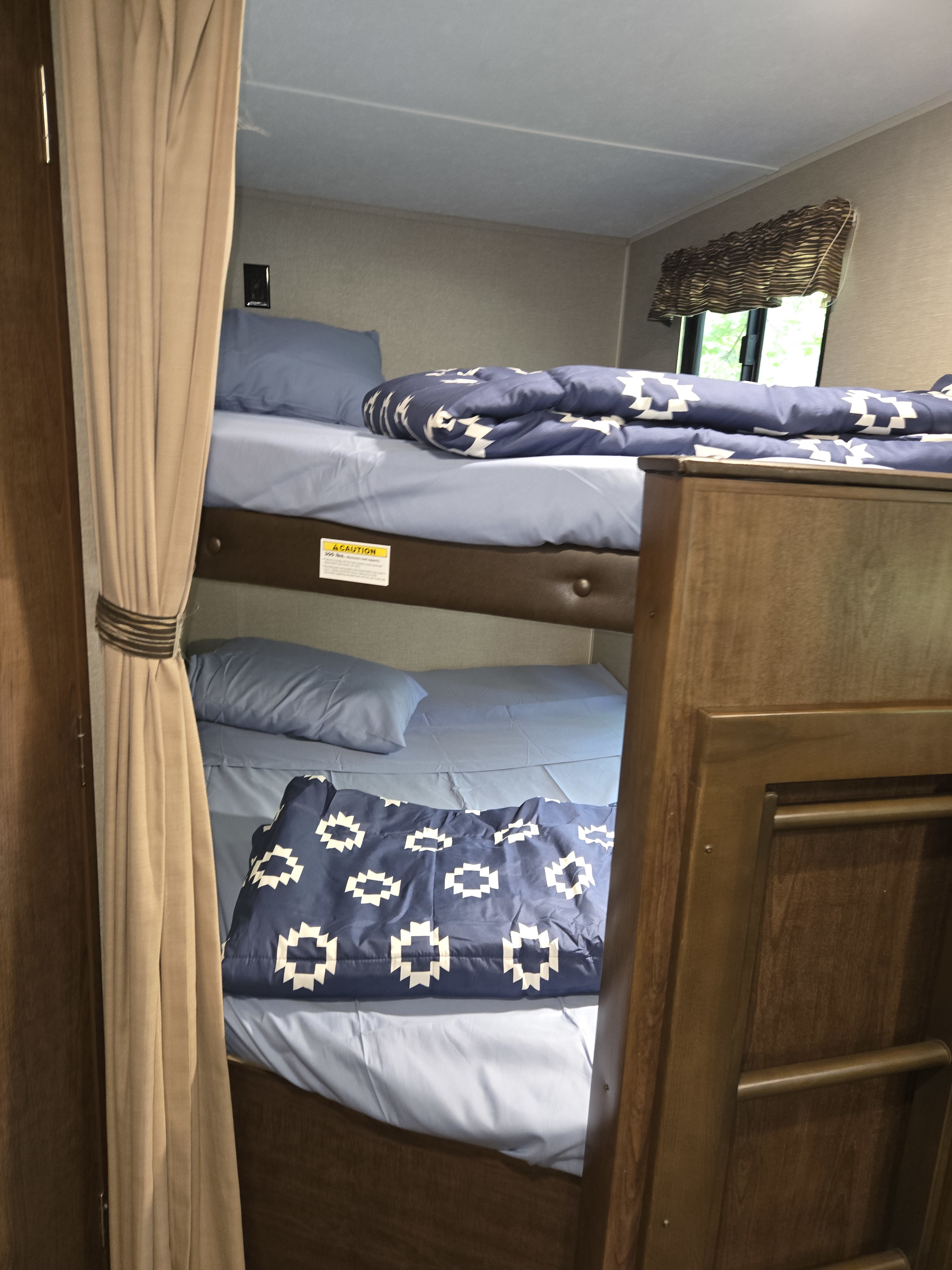 Inside an RV rental: two neatly made bunk beds with blue bedding and geometric comforters.. Keystone RV Hideout LHS 2018