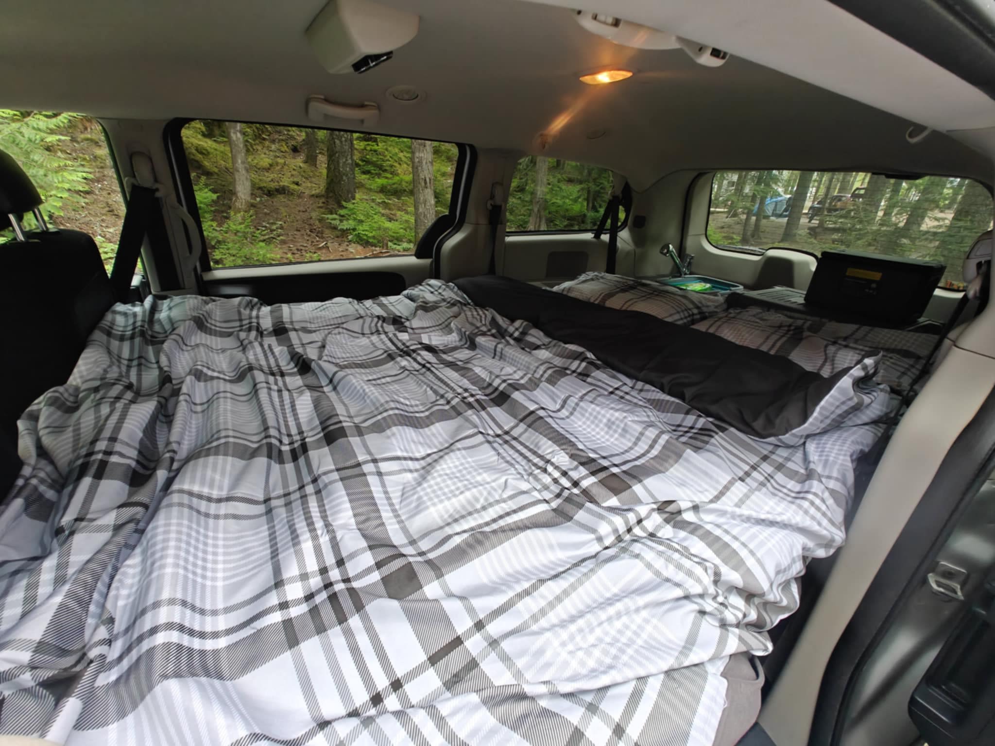 Cozy RV rental: a comfortable plaid bed inside a van, with forest views for peaceful car camping.. Dodge Grand Caravan 2011
