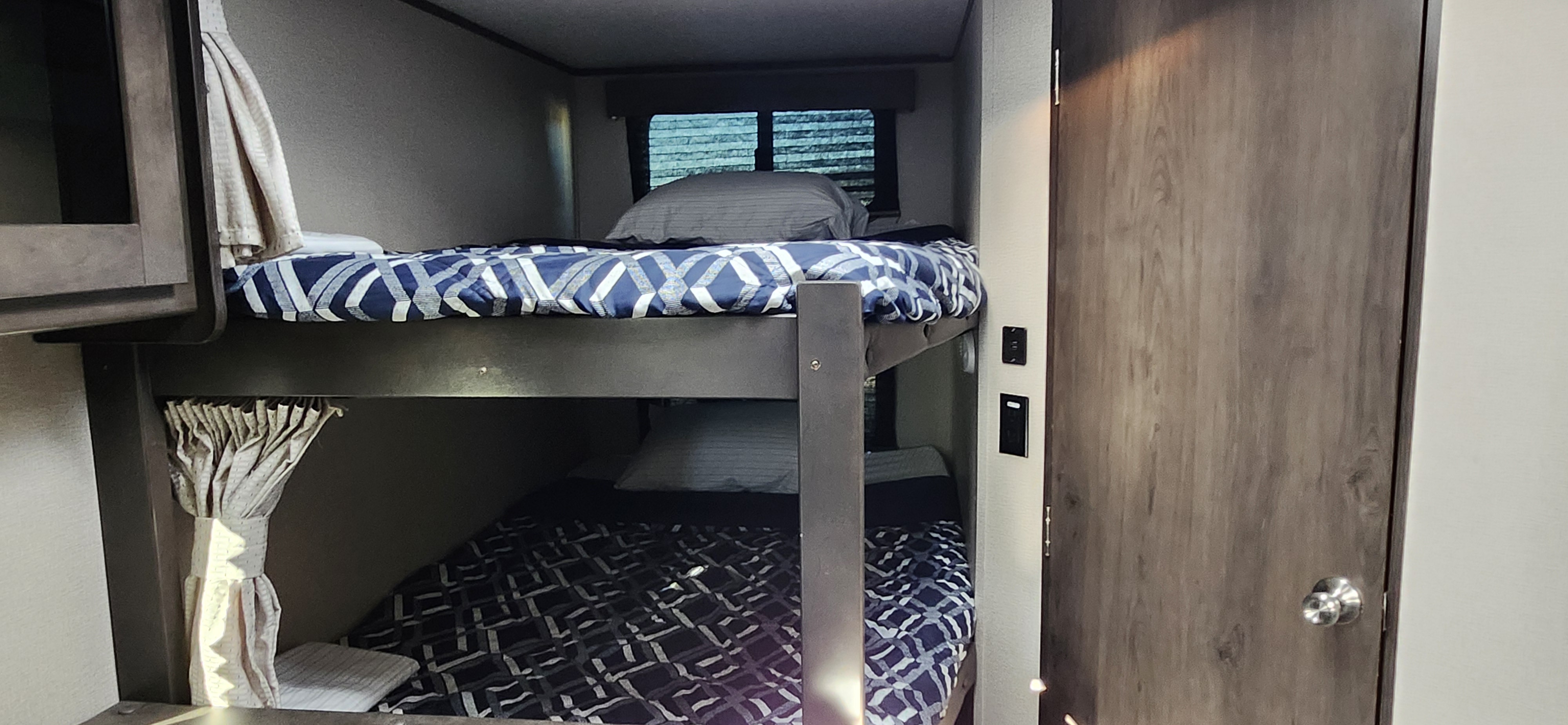 RV rental with cozy bunk beds: navy patterned bedding, window & door visible inside this travel trailer.. Grand Design Transcend Xplor 2022