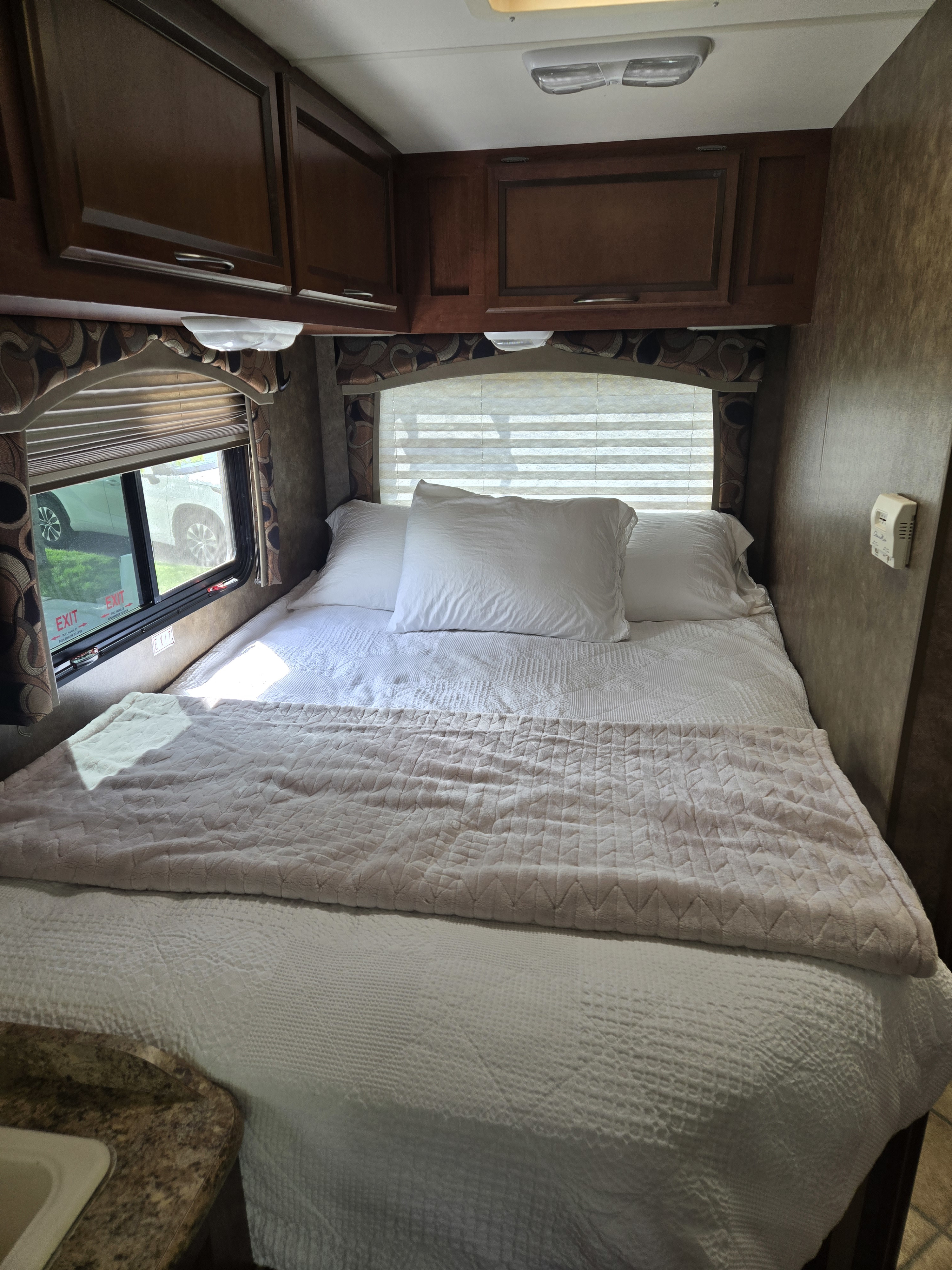 Cozy RV rental bedroom with clean white bedding, overhead cabinets, and a window. Perfect for your next adventure.. Thor Chateau 2013