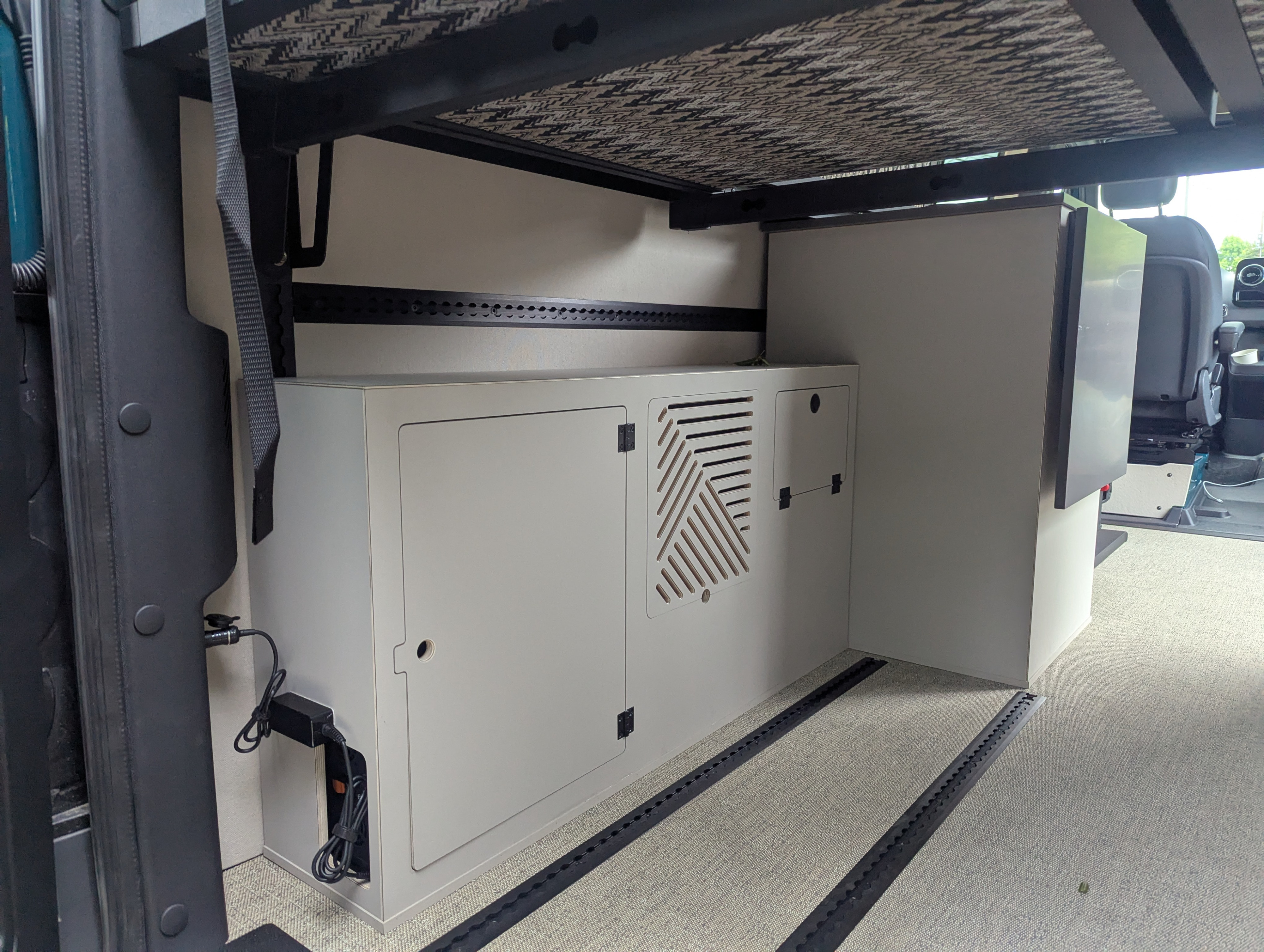 RV rental interior: Organized storage, cabinet with vent, and refrigerator under a bed frame in a camper van.. Mercedes-Benz Sprinter 2025