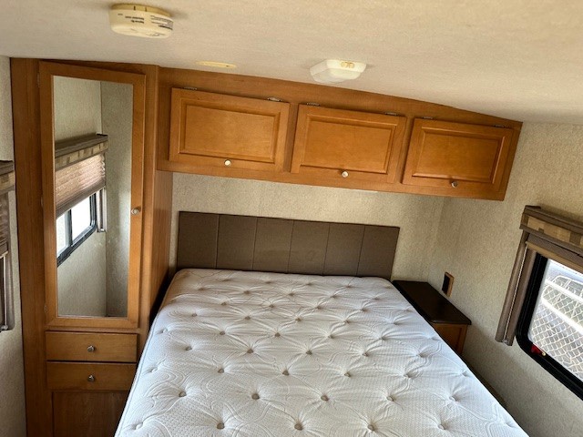 Inside an RV rental: a compact bedroom featuring a comfortable bed, overhead storage cabinets, and a mirrored wardrobe.. Itasca Sunstar 2008