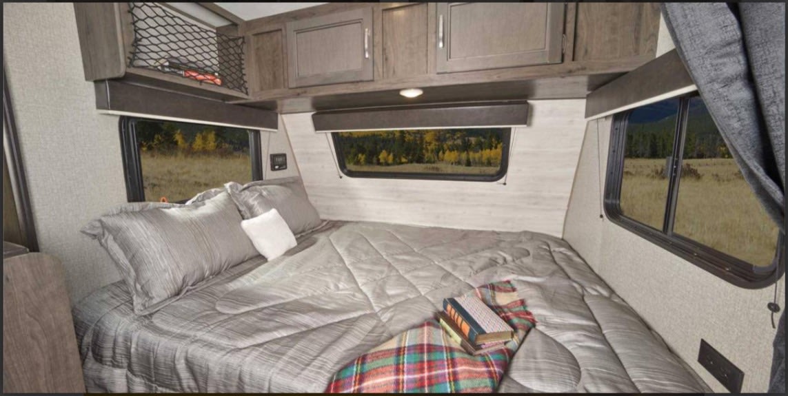 Inviting RV rental bedroom with a plush bed, overhead cabinets, and windows offering views of fall foliage and fields.. Jayco Jay Flight SLX 2021