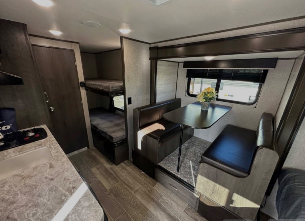 Rv rental interior: on the left, a galley kitchen and bunk beds. On the right, a dinette with bench seating, a table, and a window.. Jayco Jay Flight SLX 2021