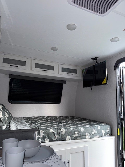 Interior of an RV rental: a comfortable bed with patterned bedding, overhead storage, a mounted TV, and a compact dining area.. Coachmen Coleman Rubicon 1628BH 2024