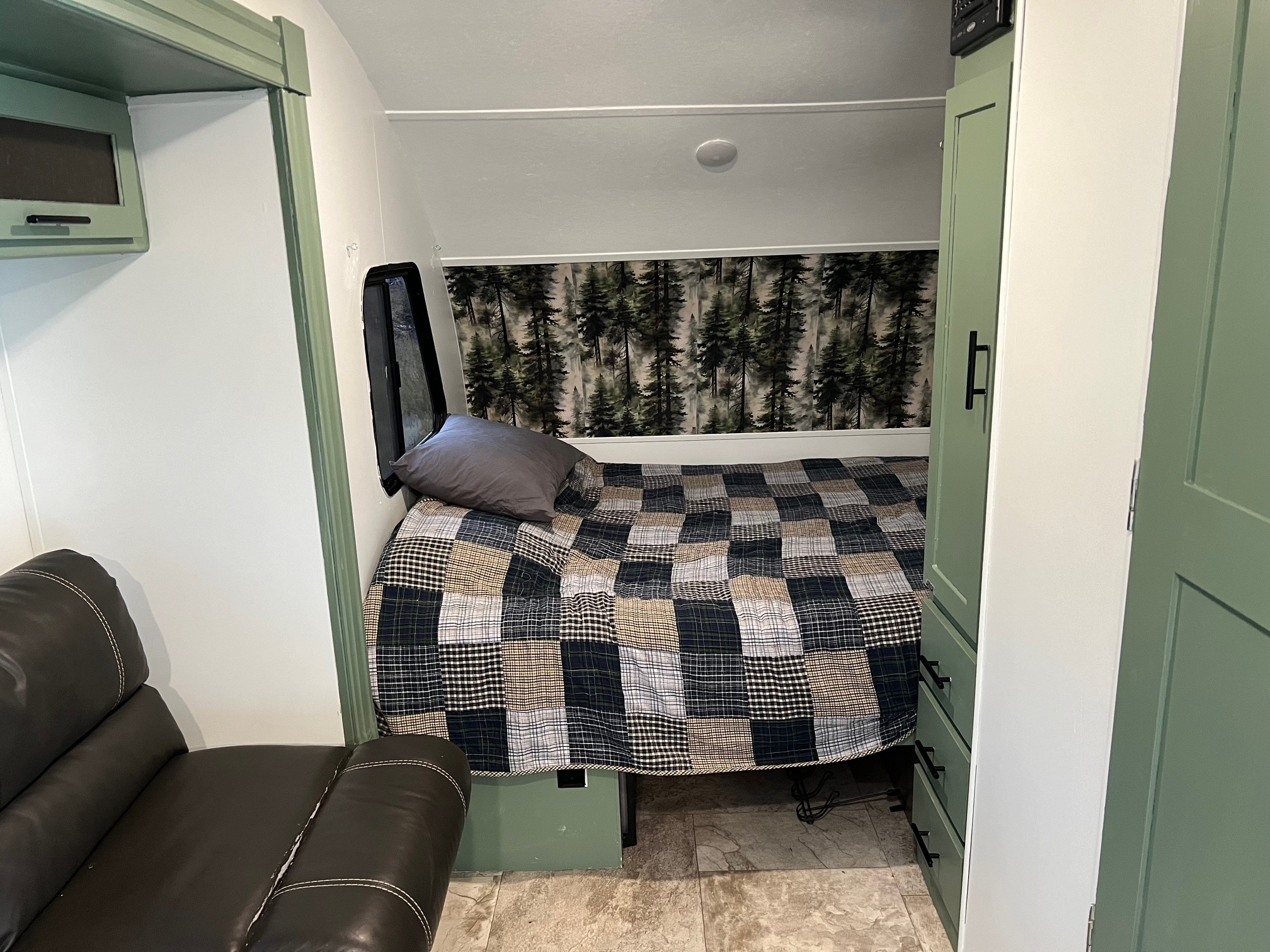 RV rental interior: cozy bedroom with a forest mural, checkered quilt, sage green built-ins, and brown recliner.. Forest River R Pod 179 2017