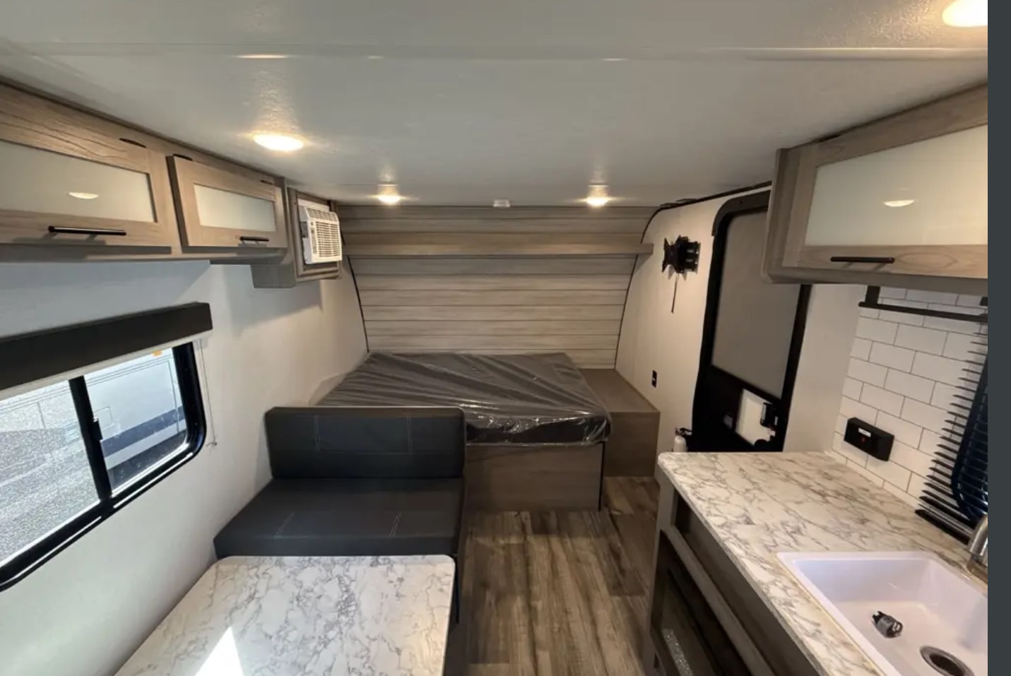 Inside an RV rental: full bed, dinette with marble-top table, kitchenette, and overhead cabinets visible.. Coleman Lantern 17b 2024