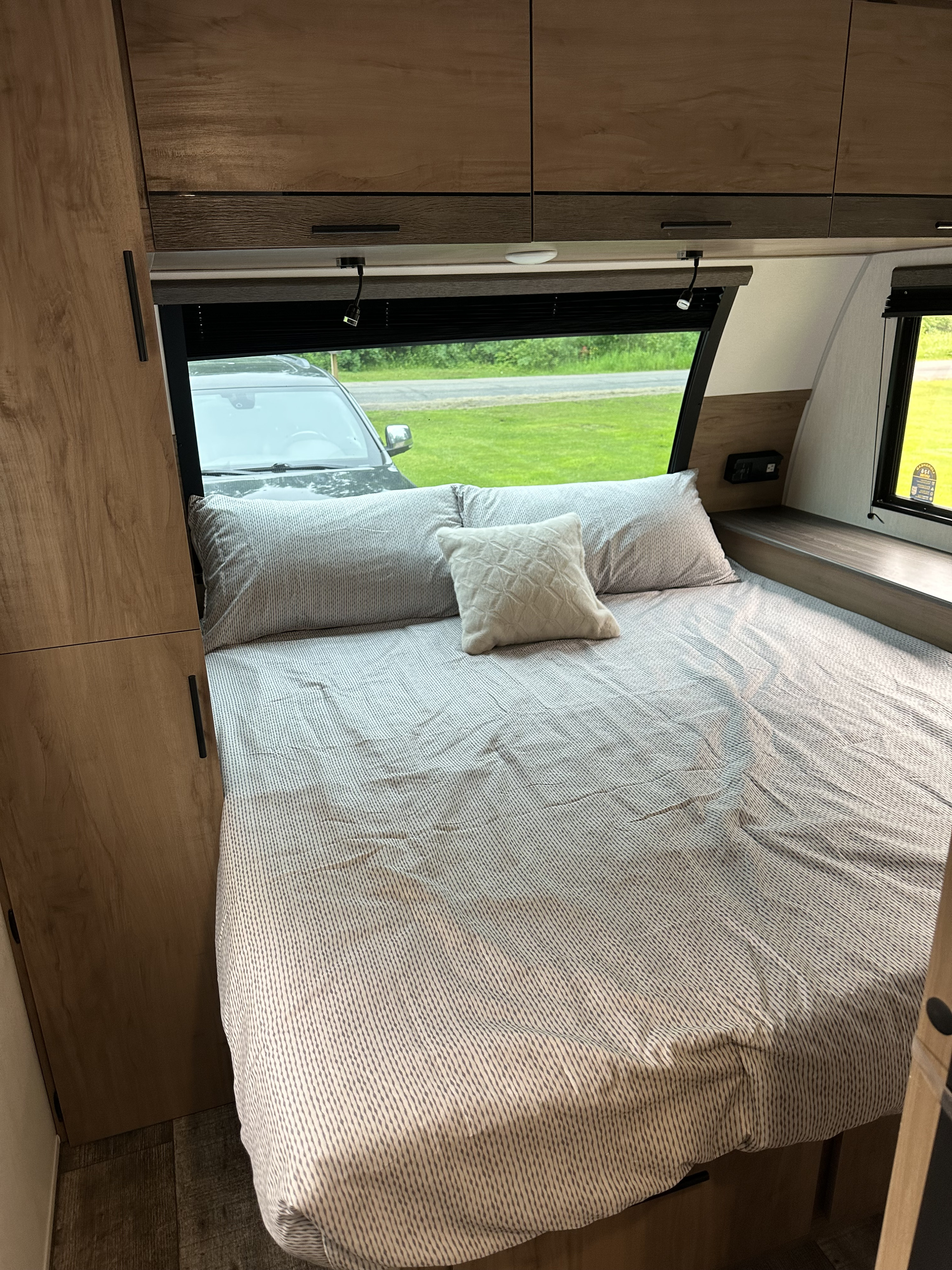 Cozy RV rental bedroom with striped bedding, overhead cabinets, and a scenic view through the window.. Forest River Campsite Ultra 26CJL 2025