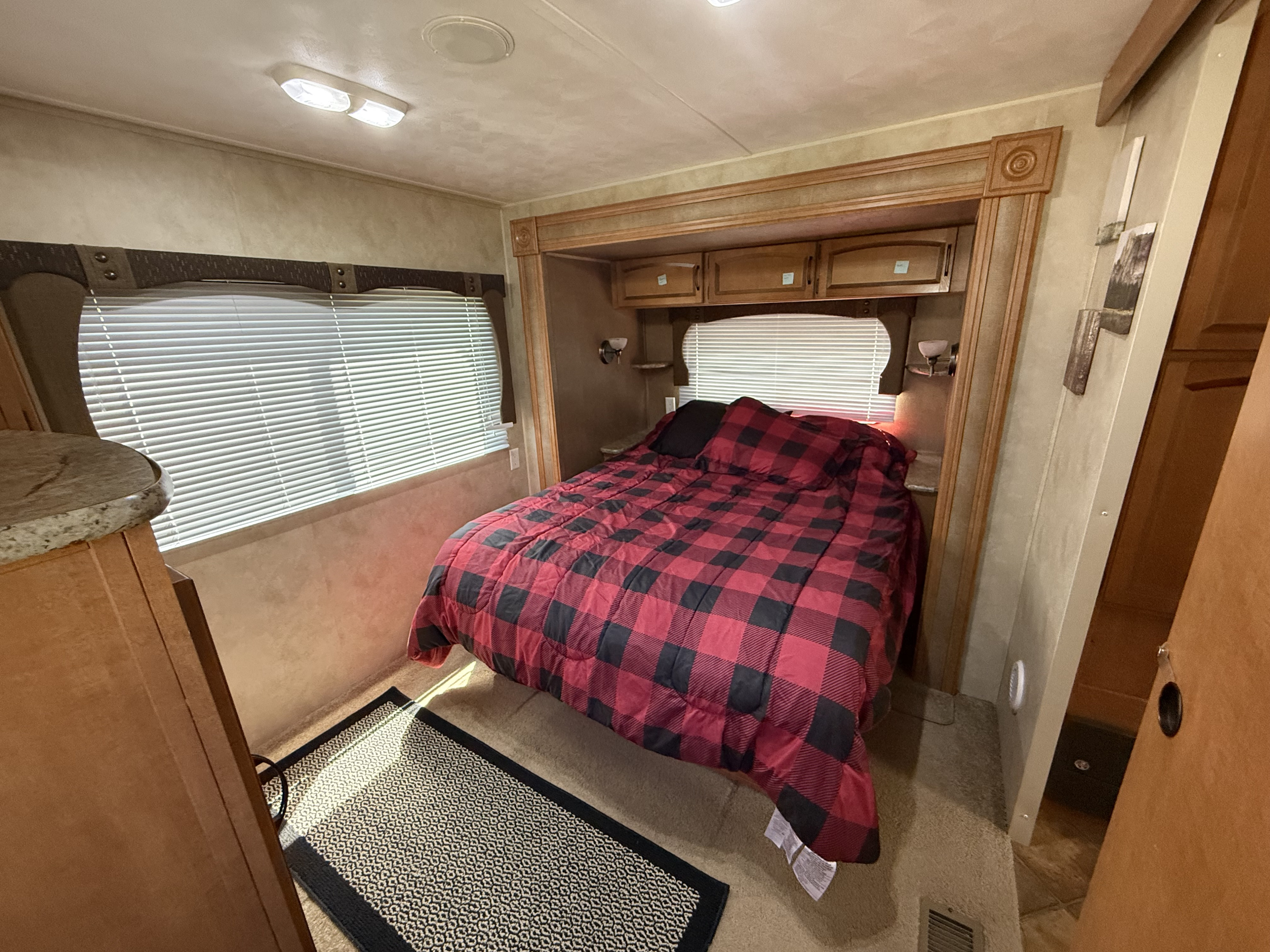 Cozy RV rental bedroom with a buffalo plaid comforter, window blinds, and storage cabinets.. Palomino Puma 2013