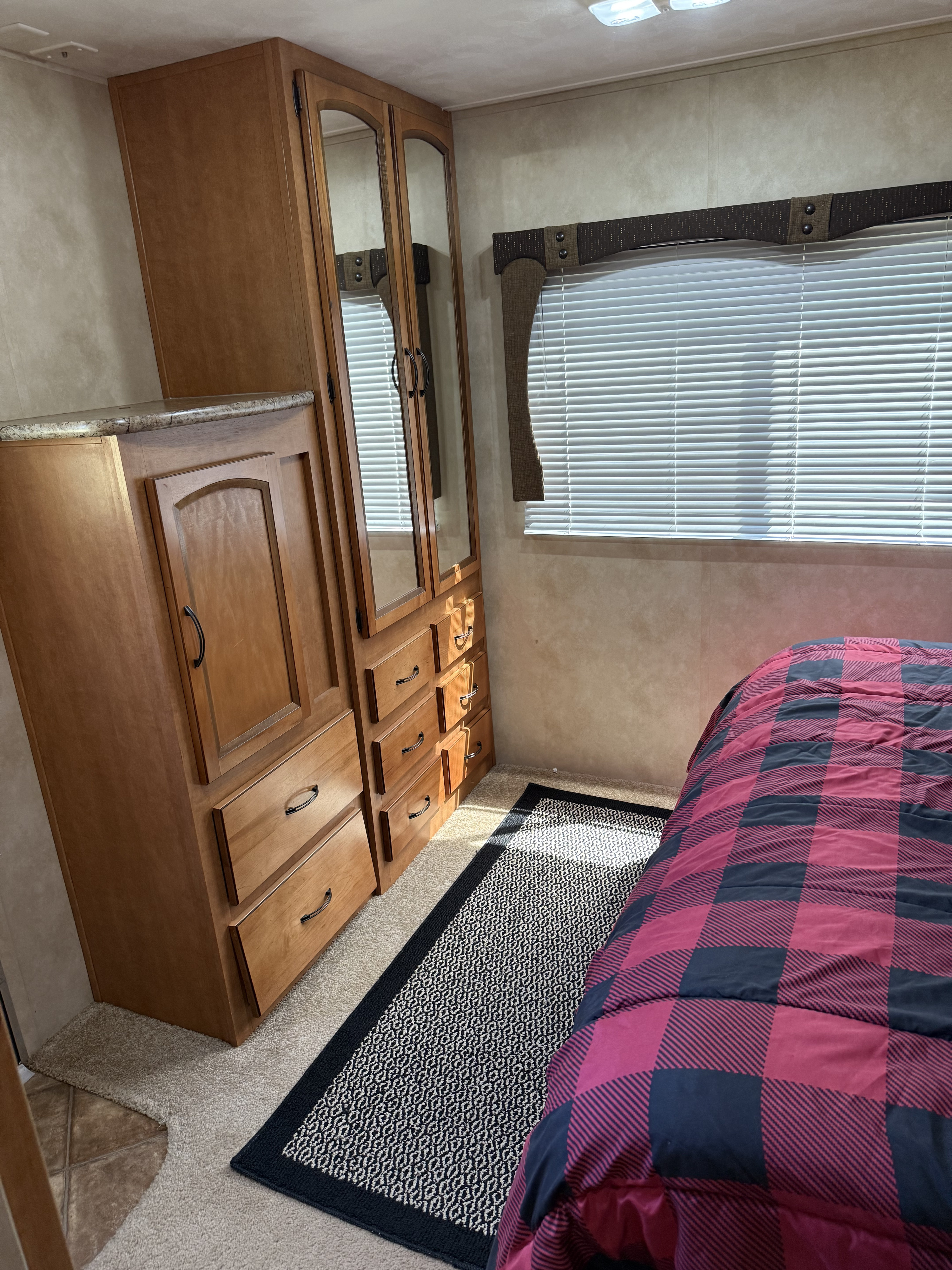 RV rental bedroom featuring a wooden wardrobe with mirrors, a red and black plaid bed, window with blinds, and patterned rug.. Palomino Puma 2013