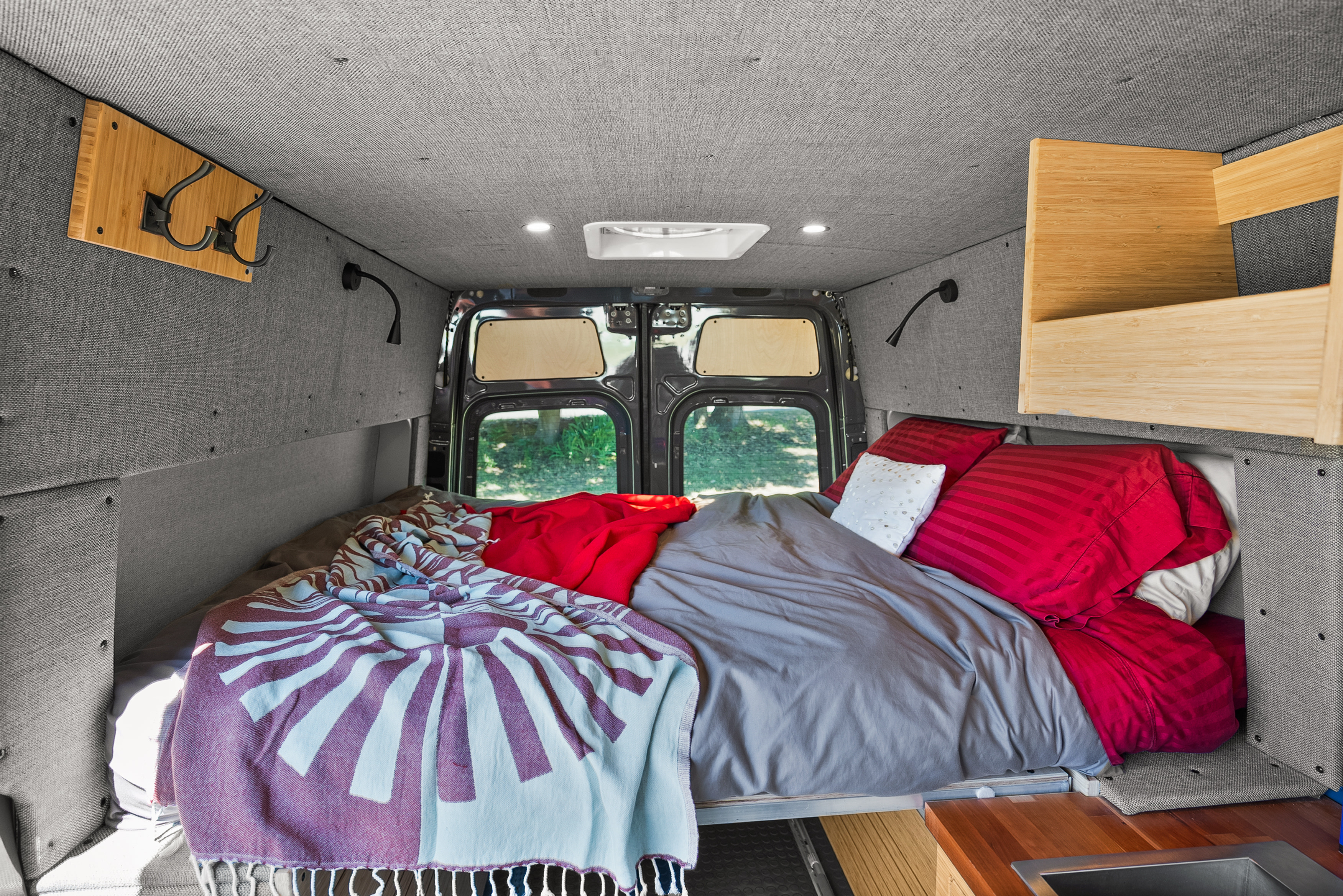 Comfortable RV rental interior showcasing a cozy bed with red and grey bedding, built-in storage, and thoughtful lighting.. Mercedes Sprinter 2022