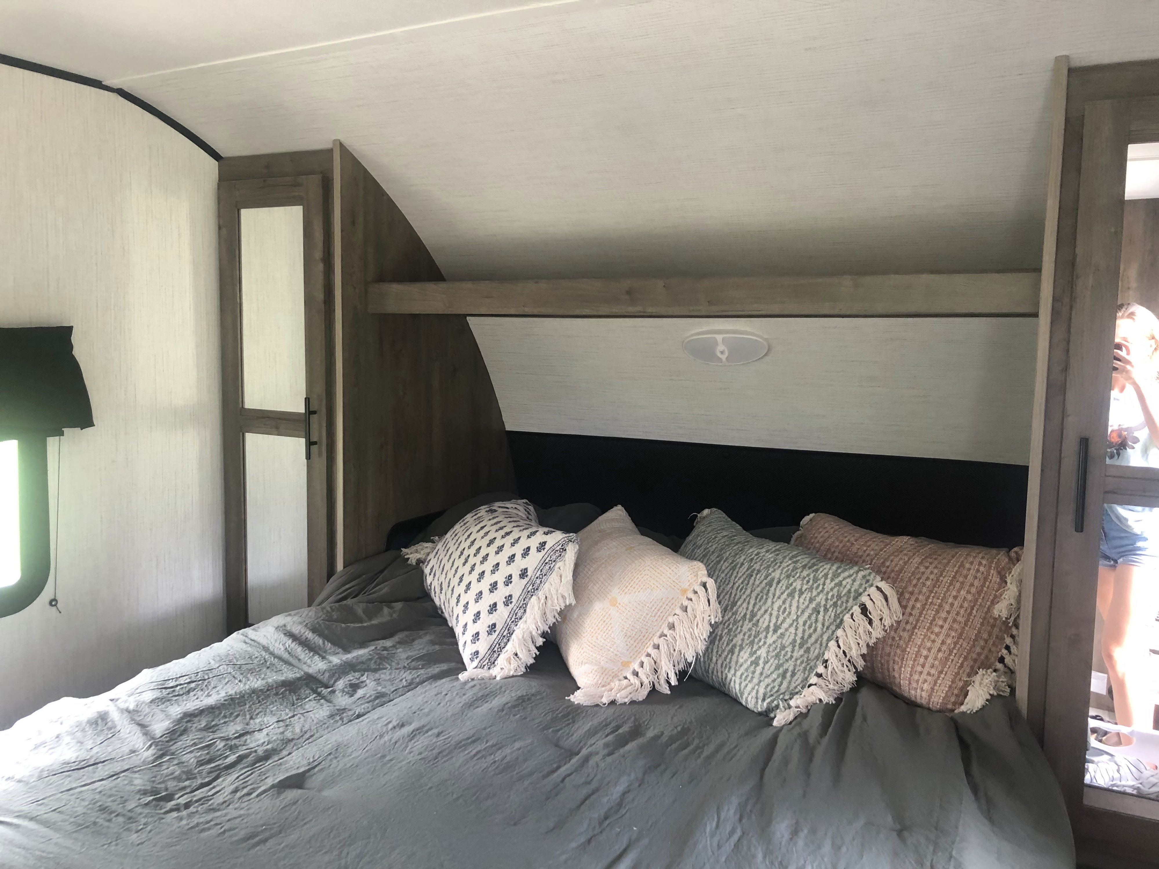 Cozy RV rental bedroom featuring dark gray bedding, decorative pillows, and built-in overhead storage with a mirrored wardrobe.. Heartland RVs Pioneer 2022