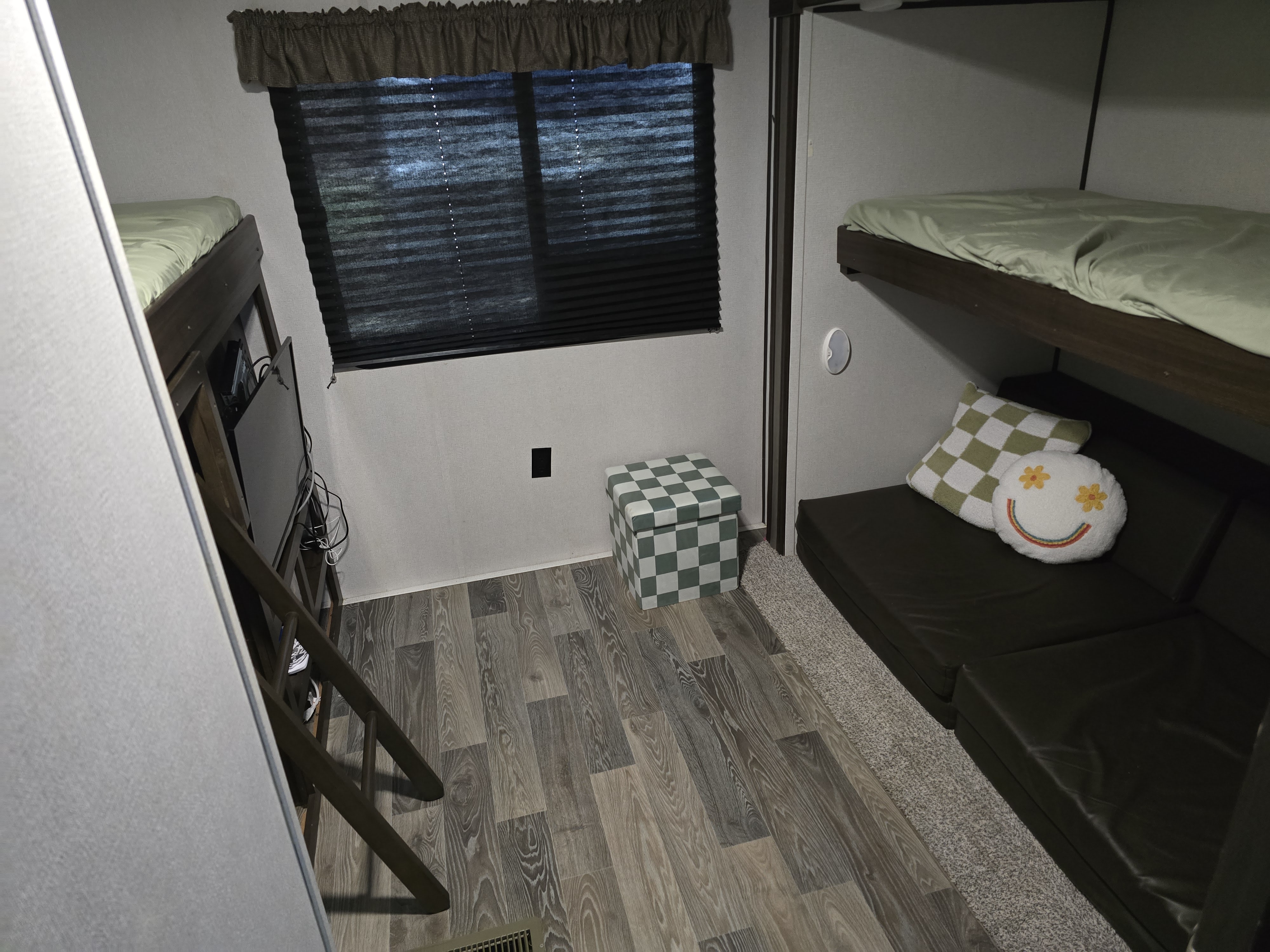 This modern RV rental bunk room features stacked beds, a comfy sofa with unique pillows, a storage ottoman, and a TV.. Keystone RV Springdale 2020
