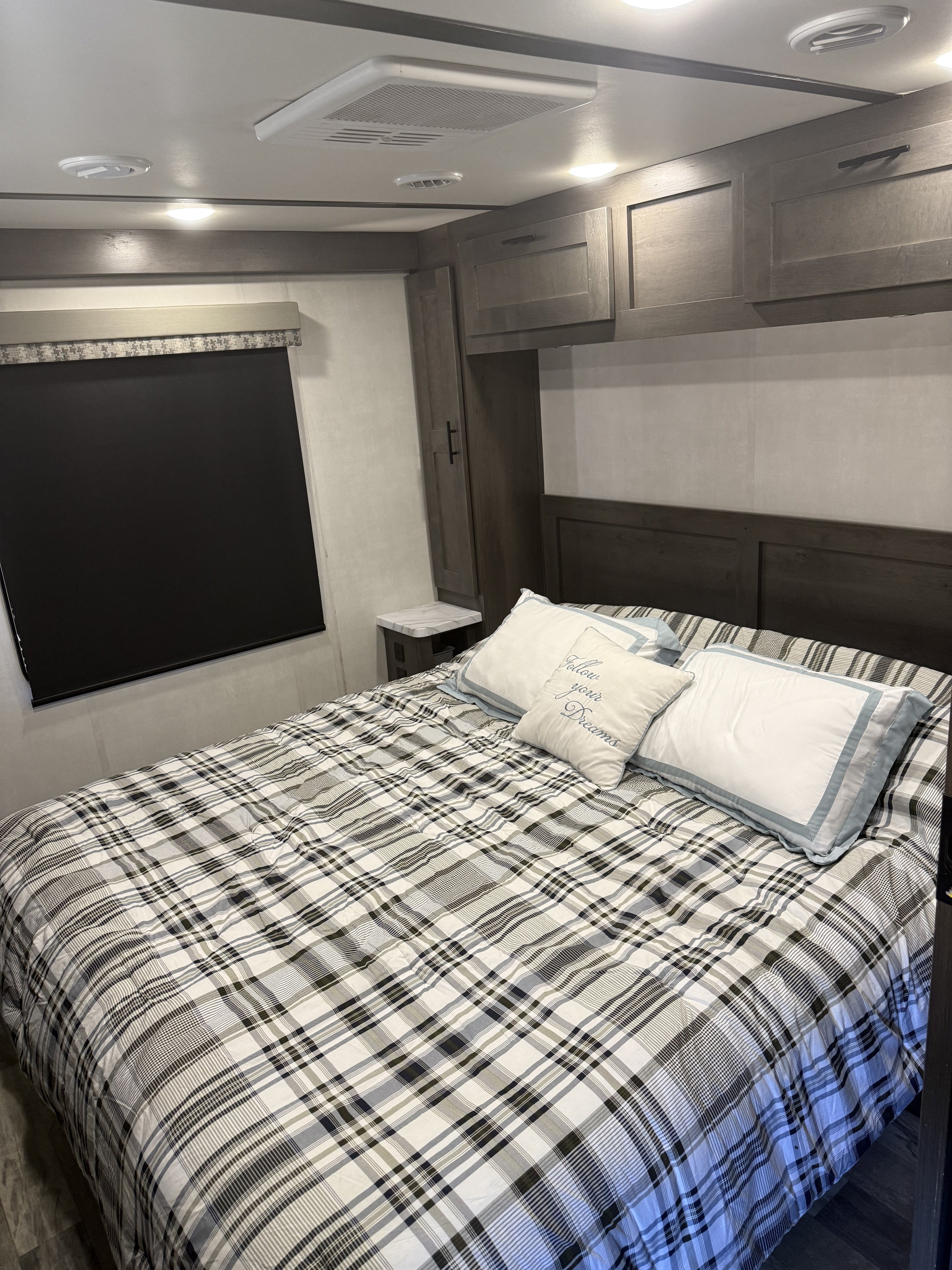 Cozy RV rental bedroom featuring a plaid bed, overhead cabinets, and a window with a blackout shade.. FR3 FR3 Motorhome 2021