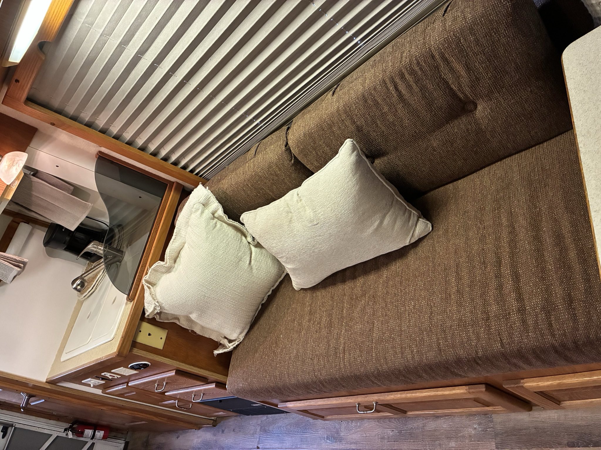 Enjoy this RV rental living space: brown sofa, light pillows, compact kitchenette, and wooden accents.. Born Free Born Free Motorhome 2005