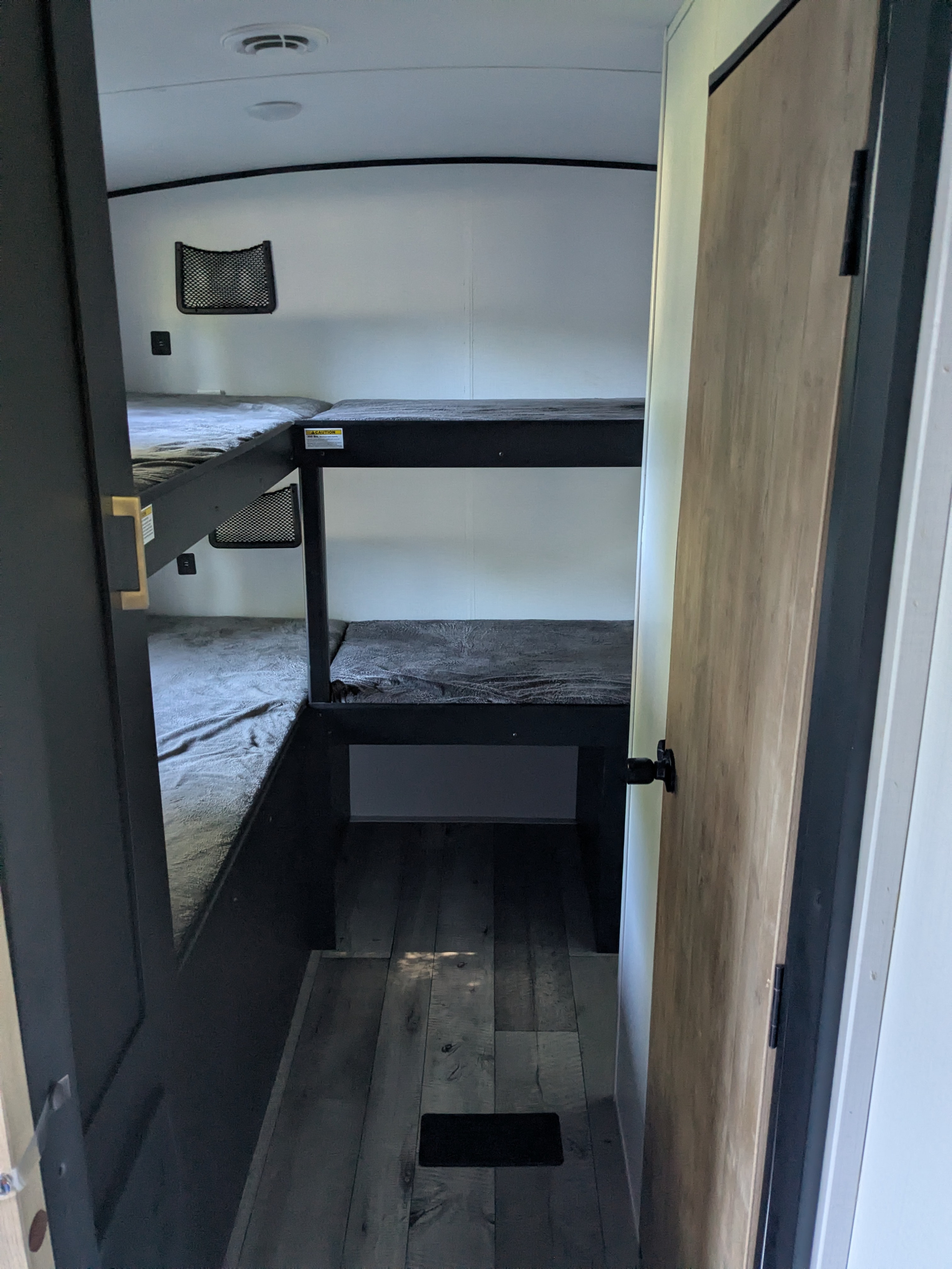 Inside an RV rental, a compact bunkhouse offers four beds with grey blankets. Dark frames support the bunks, complemented by wood-look flooring.. Keystone RV Springdale 2022