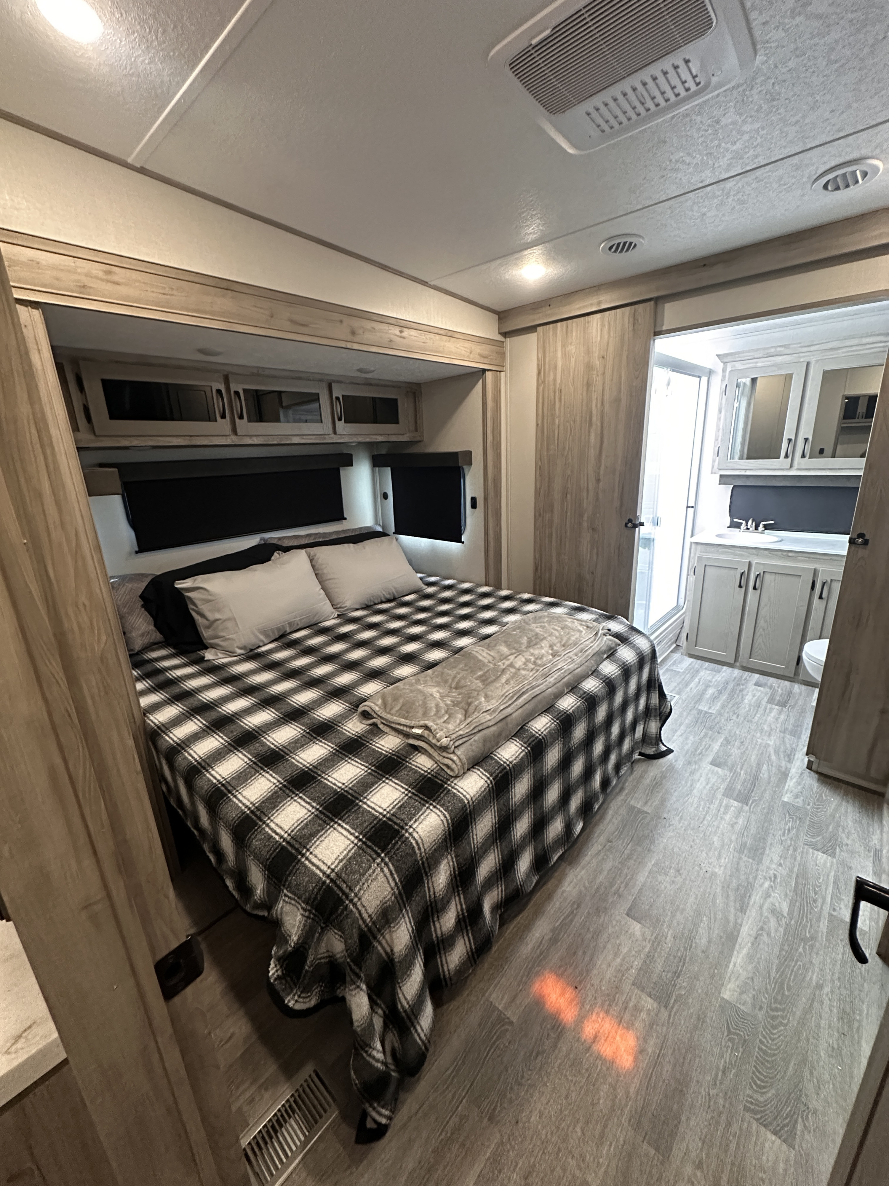 Modern RV rental interior featuring a cozy bedroom with a plaid bedspread and an adjacent full bathroom.. Coachman chaparral 355 fbx 2024