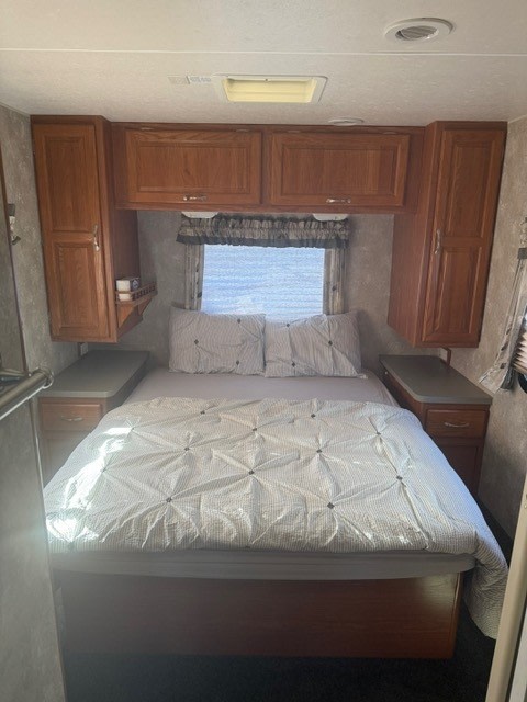 This compact RV rental bedroom features a comfortable bed, overhead cabinets, and side storage, perfect for your travels.. Coachmen Mirada Deluxe/Premier 2004
