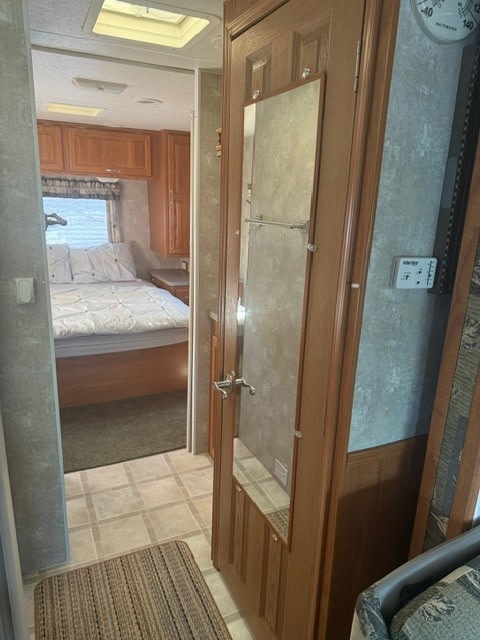 RV rental interior: View into bedroom with a bed, wooden cabinets, tiled floor, and a mirrored closet door.. Coachmen Mirada Deluxe/Premier 2004