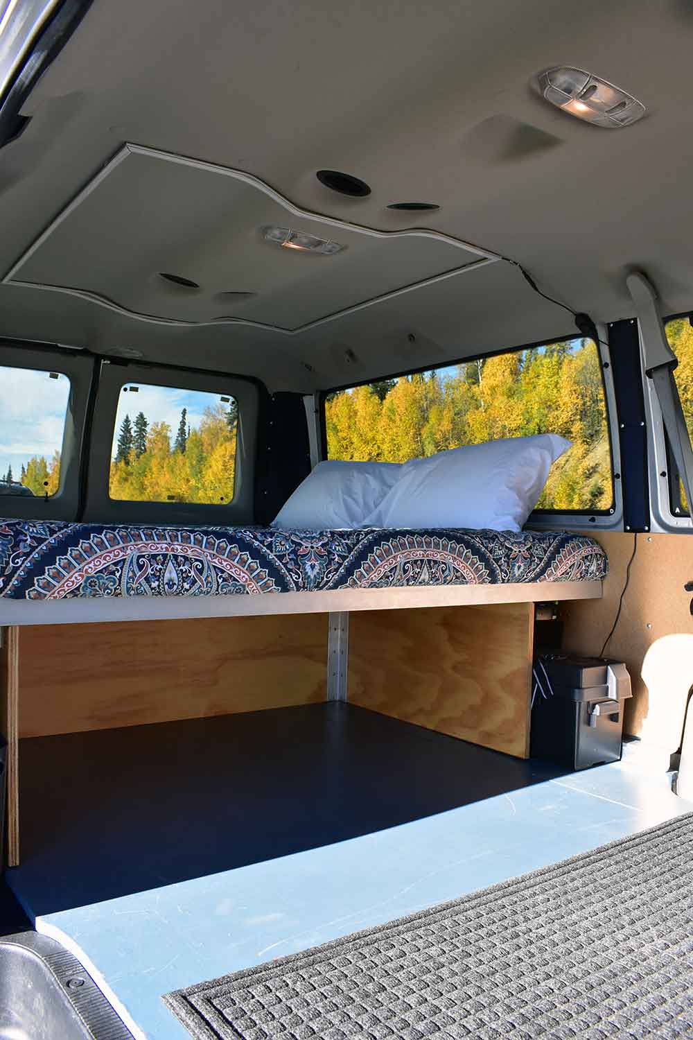 Inside a cozy camper van ready for your next RV rental adventure: elevated bed with storage below, framed by autumn trees.. Ford Ford E350 2014