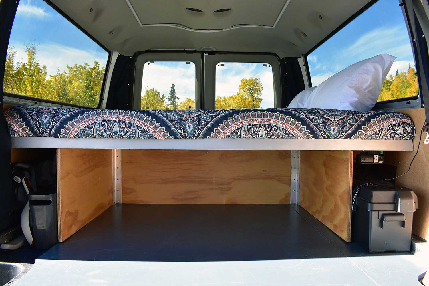 RV rental camper van rear: a patterned bed with under-bed storage, power unit, and tree-lined window views.. Ford Ford E350 2014