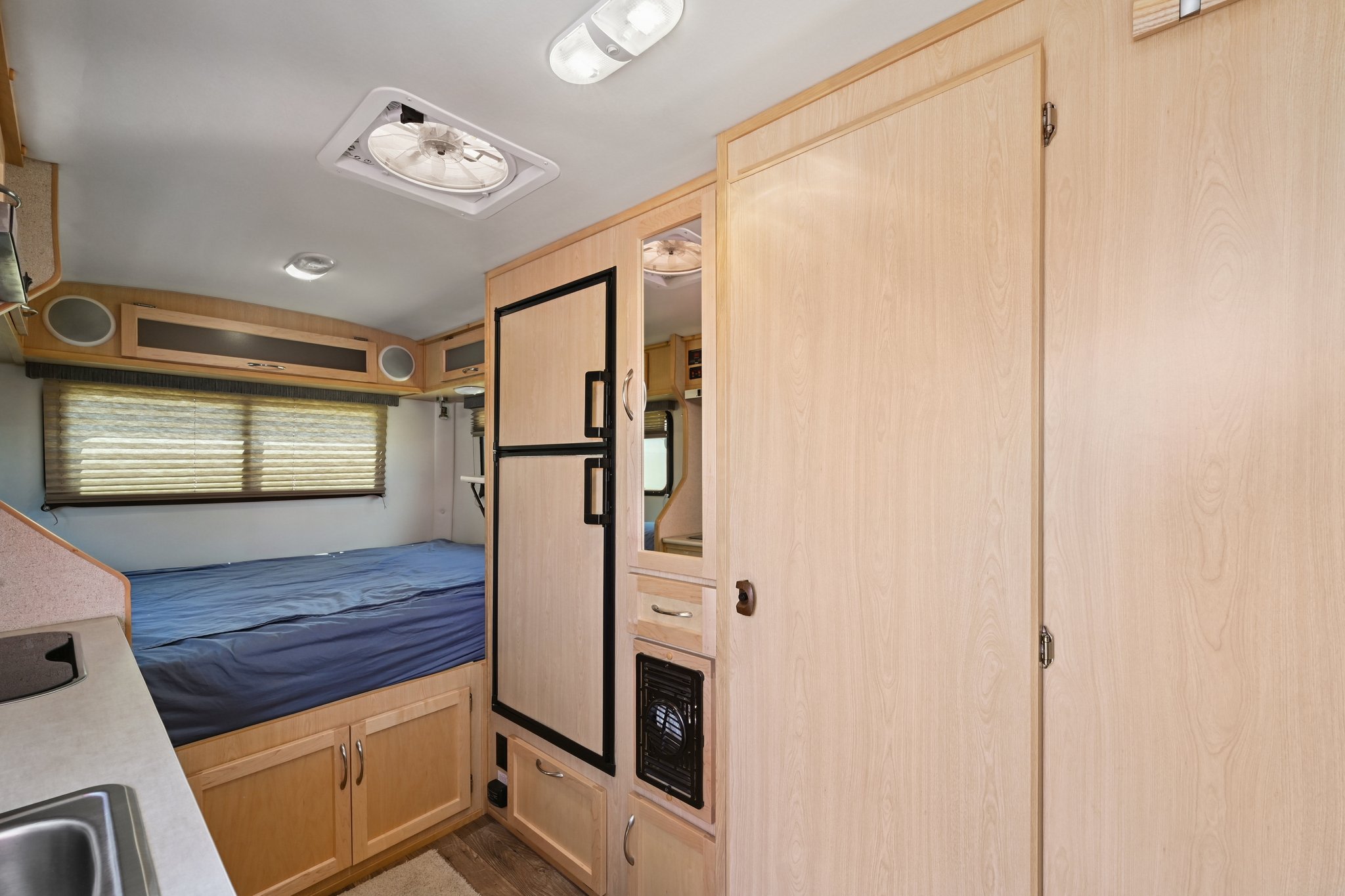 Interior of an RV rental: compact space featuring a blue-covered bed, small kitchen sink, refrigerator, and wooden storage.. Escape Trailer Escape Trailer Trailer 2021