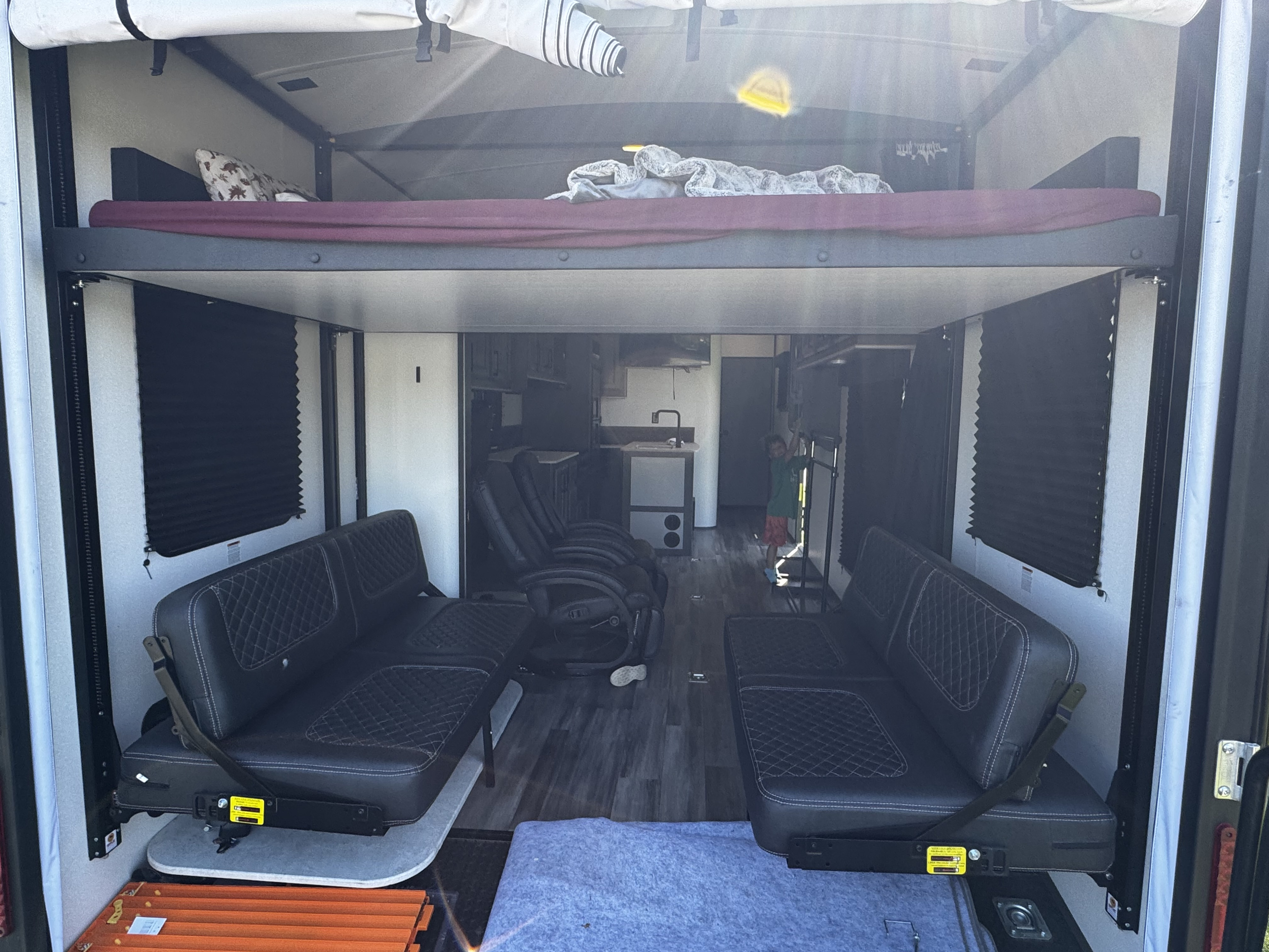 Spacious RV rental toy hauler interior. Features a raised bunk bed, two lower sofas, and a kitchen. A child is in the back.. Heartland Fuel 287 2021