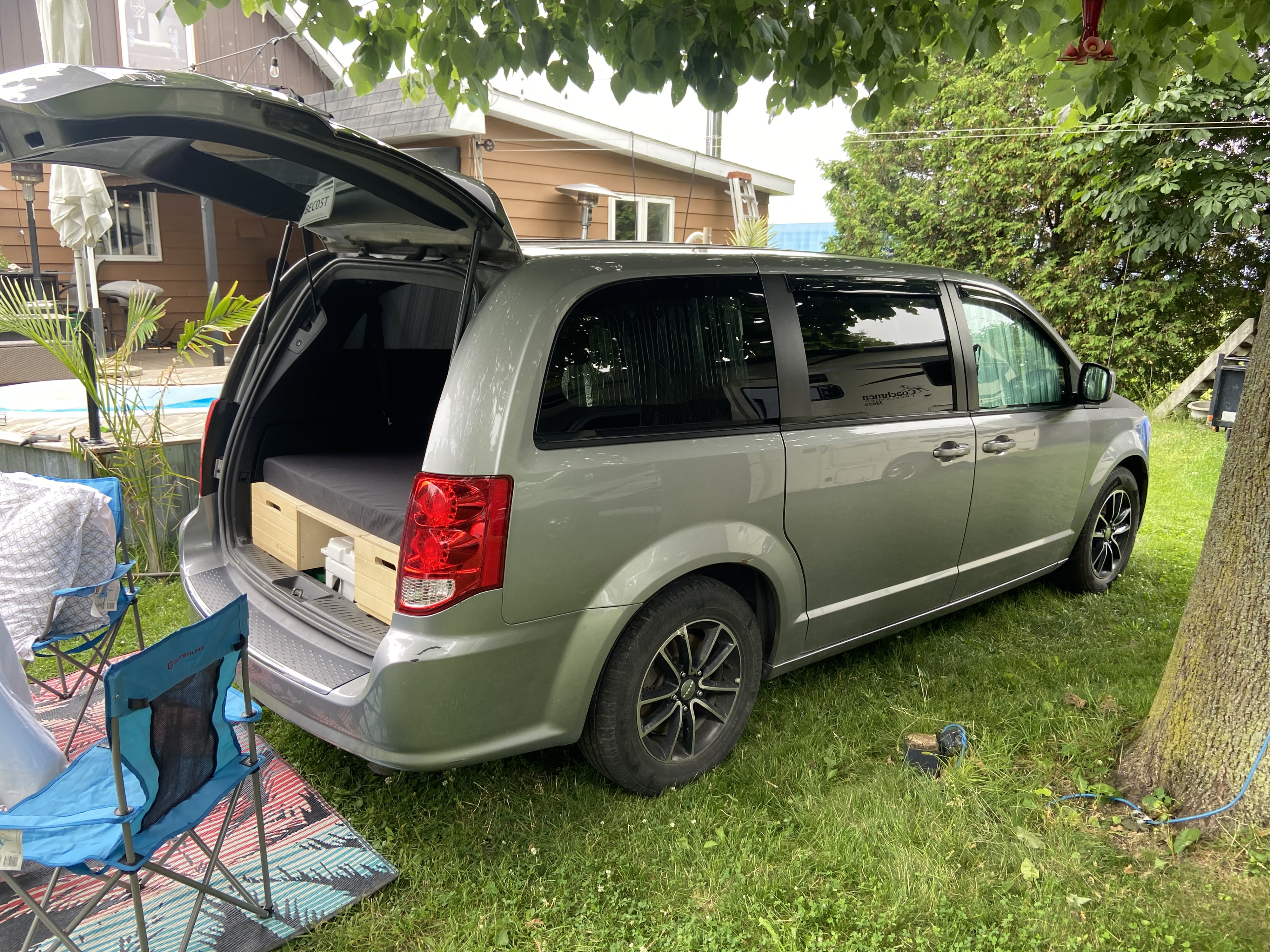 Light gray converted minivan camper, ideal for an rv rental, parked on grass with camping chairs and an open hatch.. Dodge Caravan GT 2018